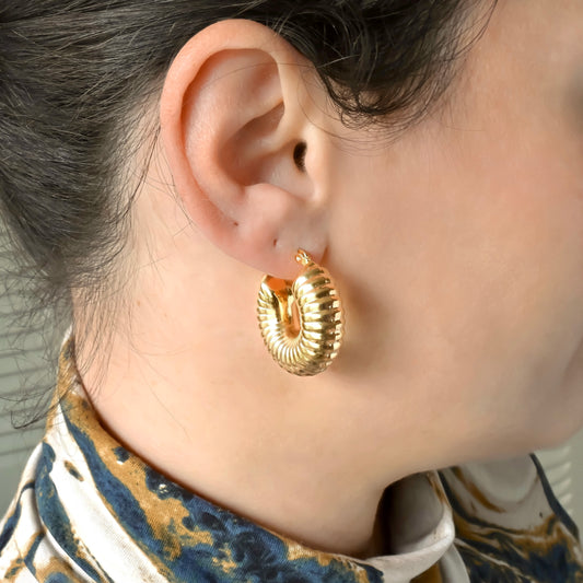 Chunky ribbed Gold hoop earrings worn by a person with a blurred background