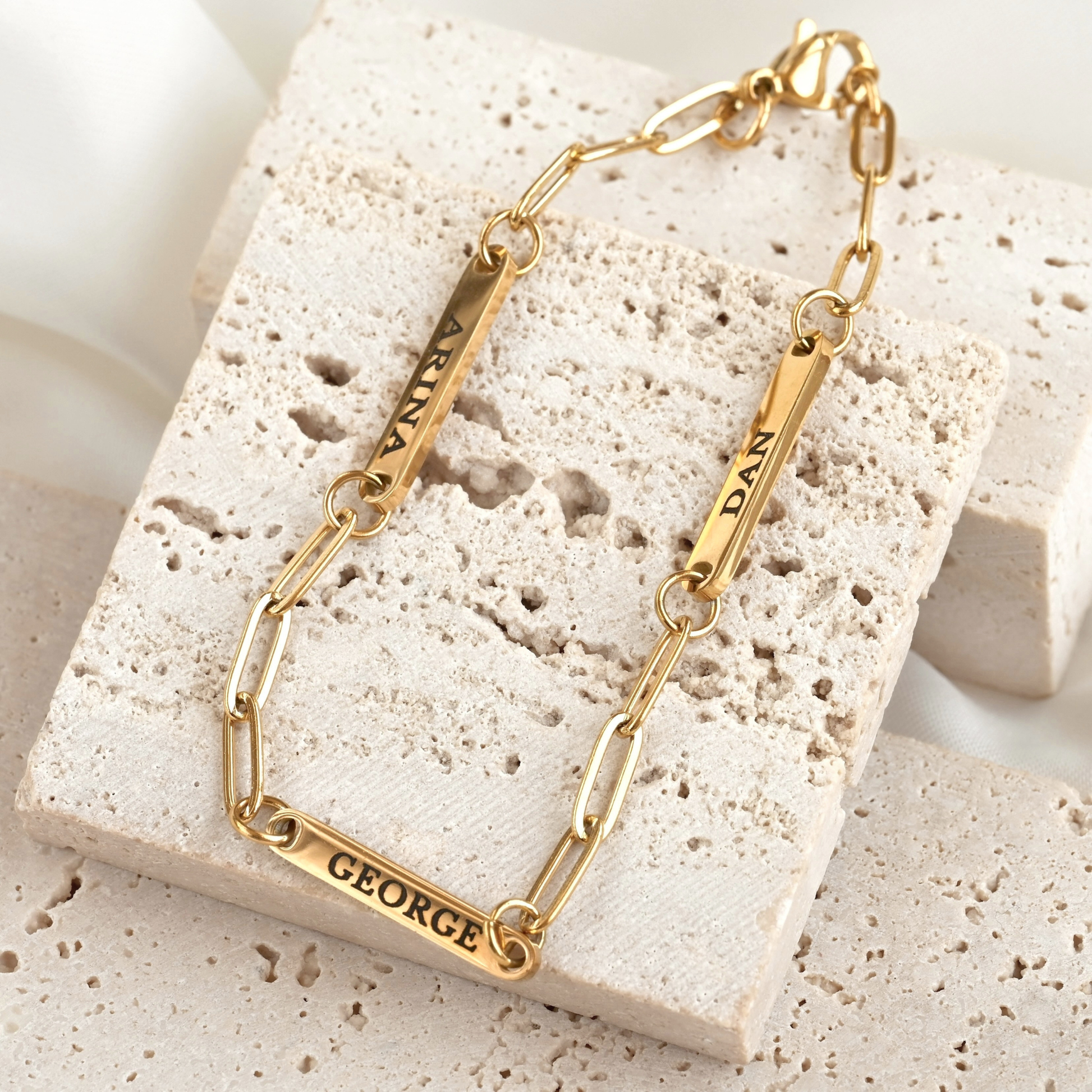 Gold  paperclip name bar bracelet with custom name engravings on a textured stone surface