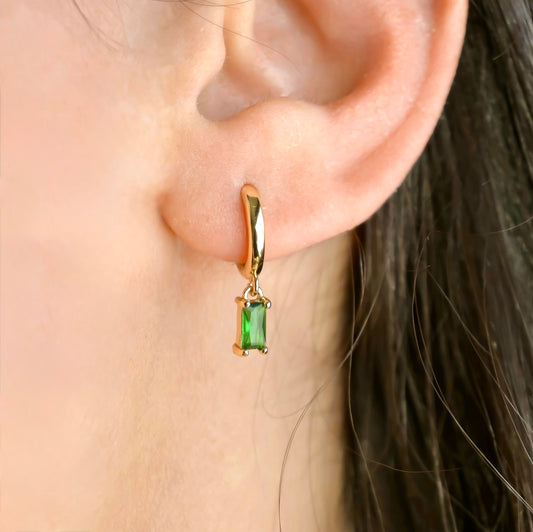 Gold huggie earring with a green gemstone worn by a person