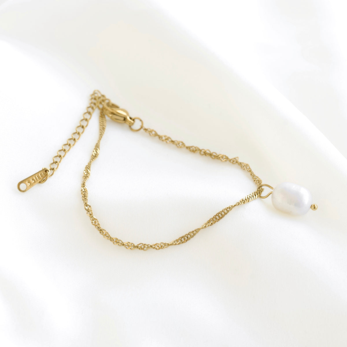 A dainty gold chain bracelet with an adjustable lobster clasp and a single baroque-style white freshwater pearl, displayed on a soft white fabric background.