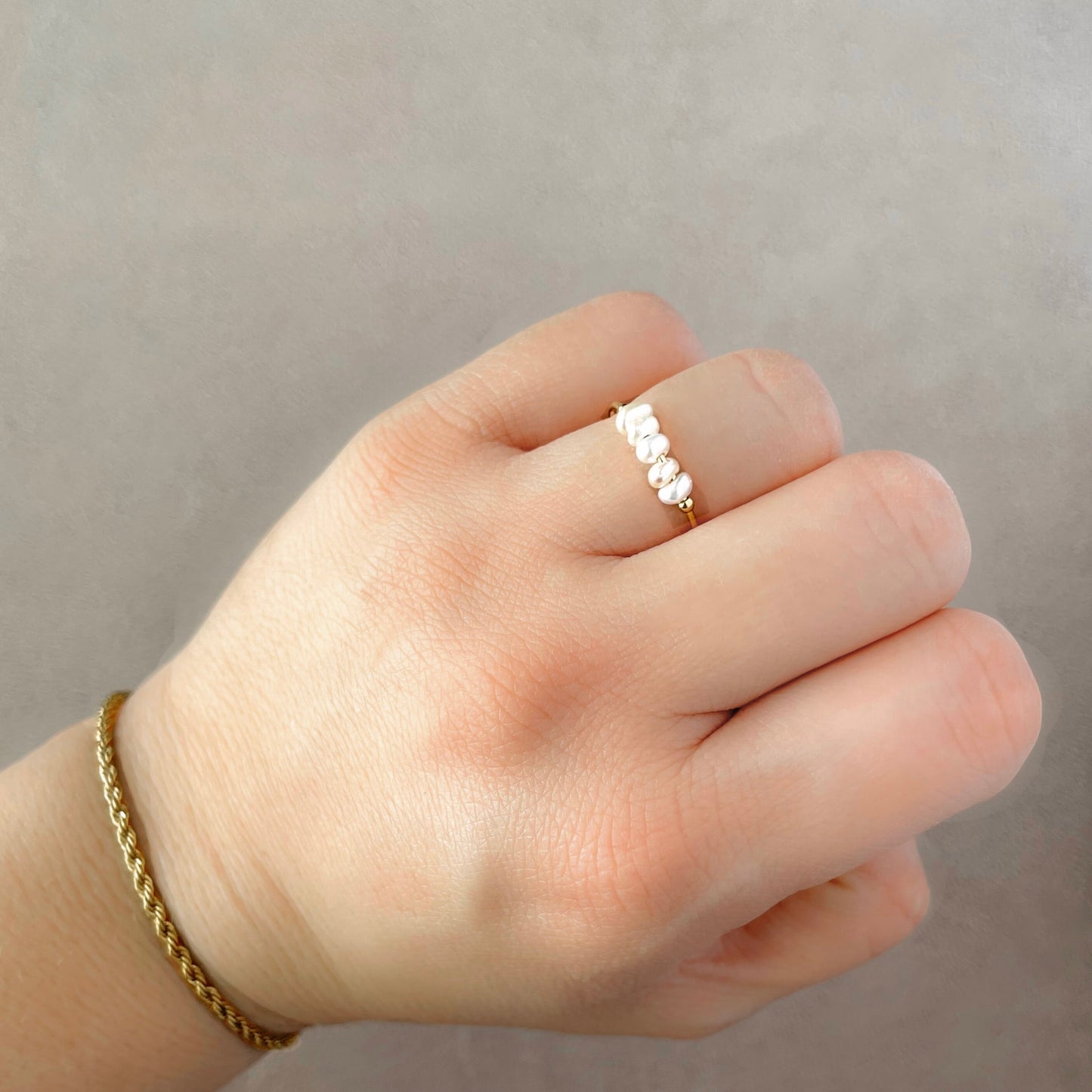 Hand wearing a delicate pearl ring with a plain background