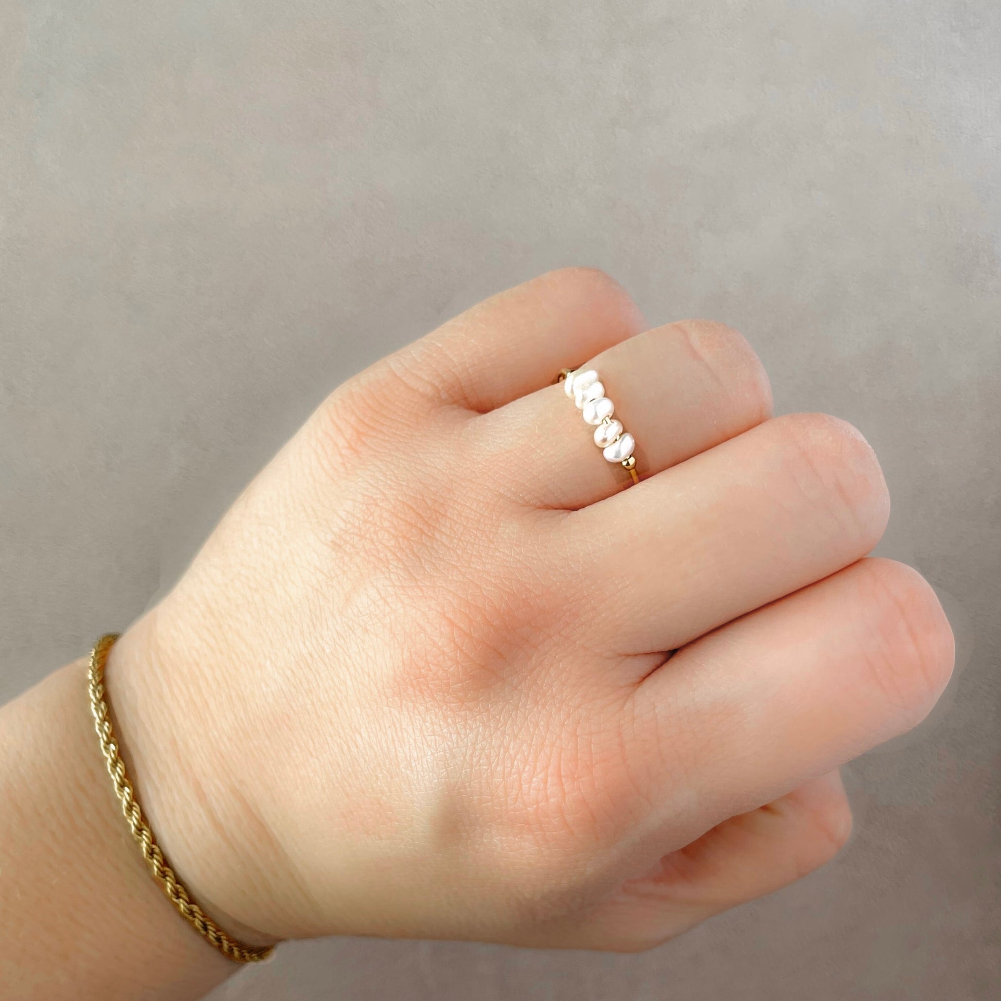 Hand wearing a delicate pearl ring with a plain background