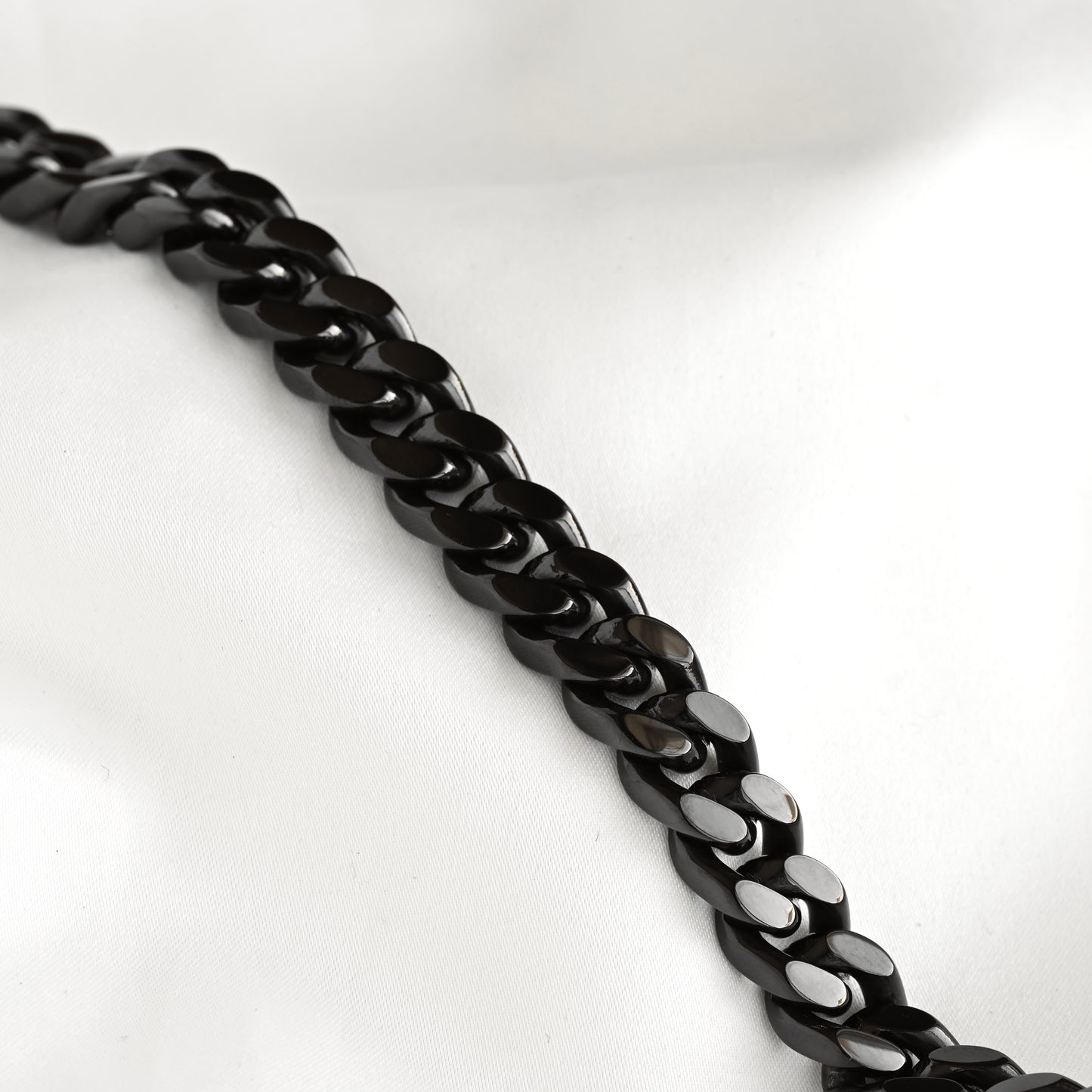 A close-up of a glossy black curb chain laid diagonally across a white fabric background.