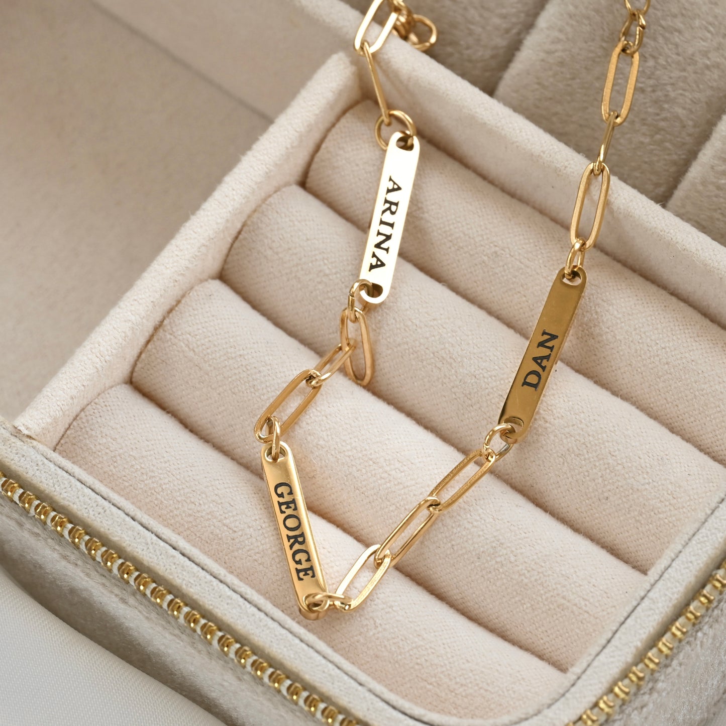Gold paperclip bracelet with engraved names on a beige jewelry box