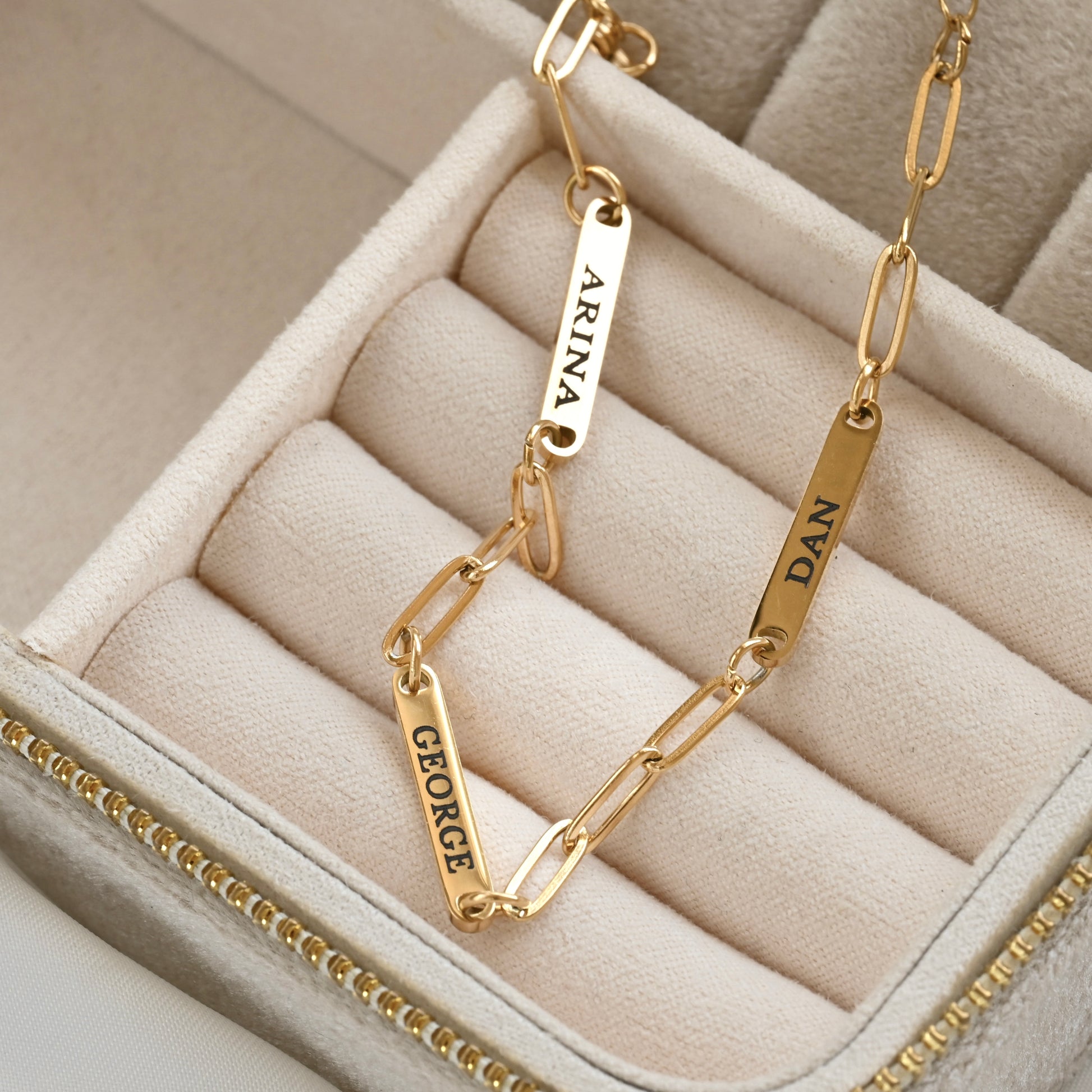Gold paperclip bracelet with engraved names on a beige jewelry box