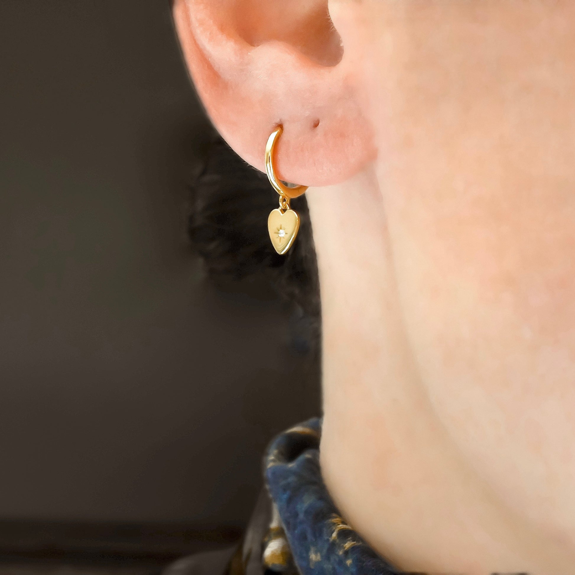 Gold  heart hoop earring worn by a person with a blurred background