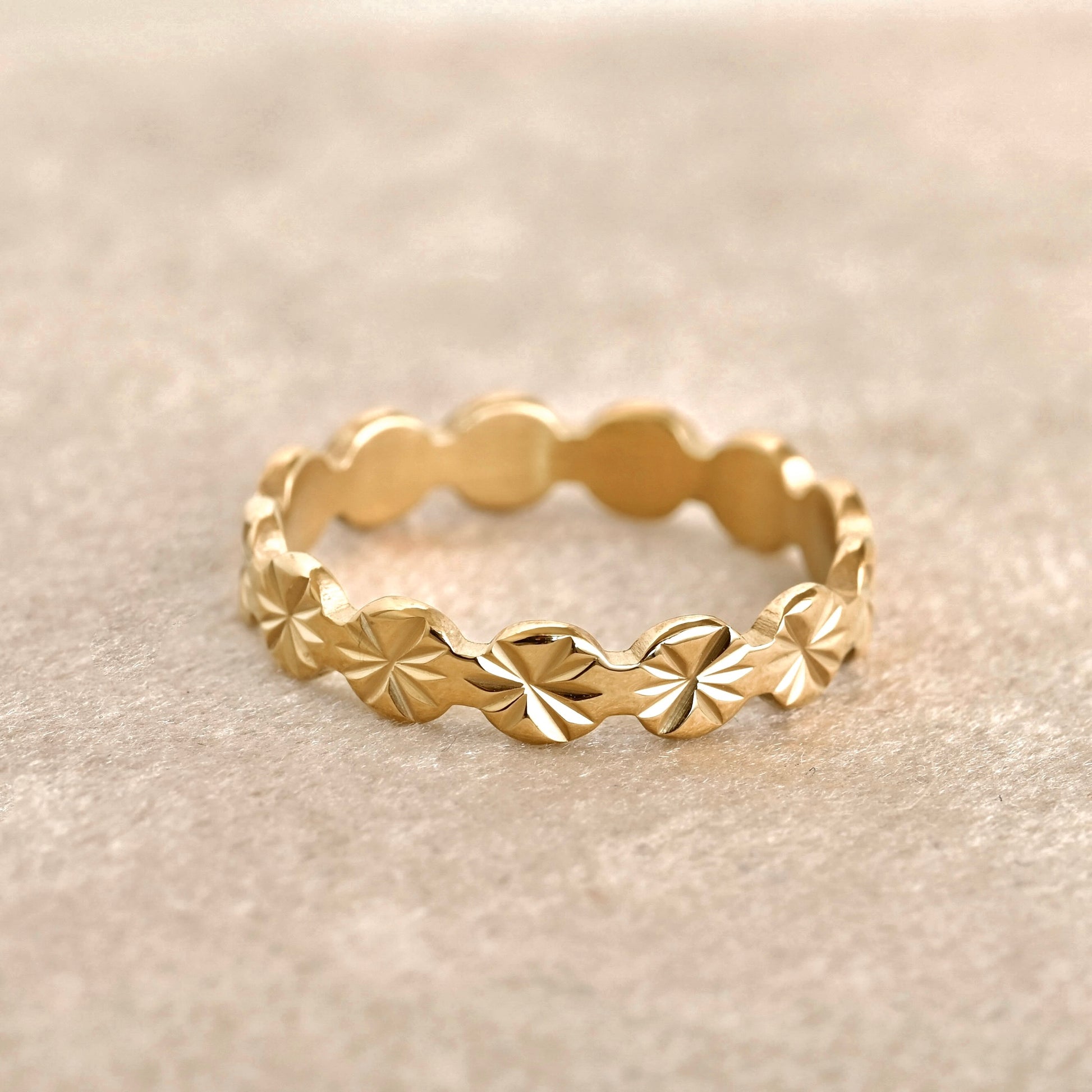 Gold ring with sunburst pattern on a beige background