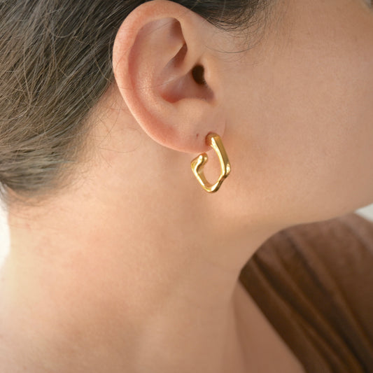 Gold molten hoop earring worn by a person with a neutral background