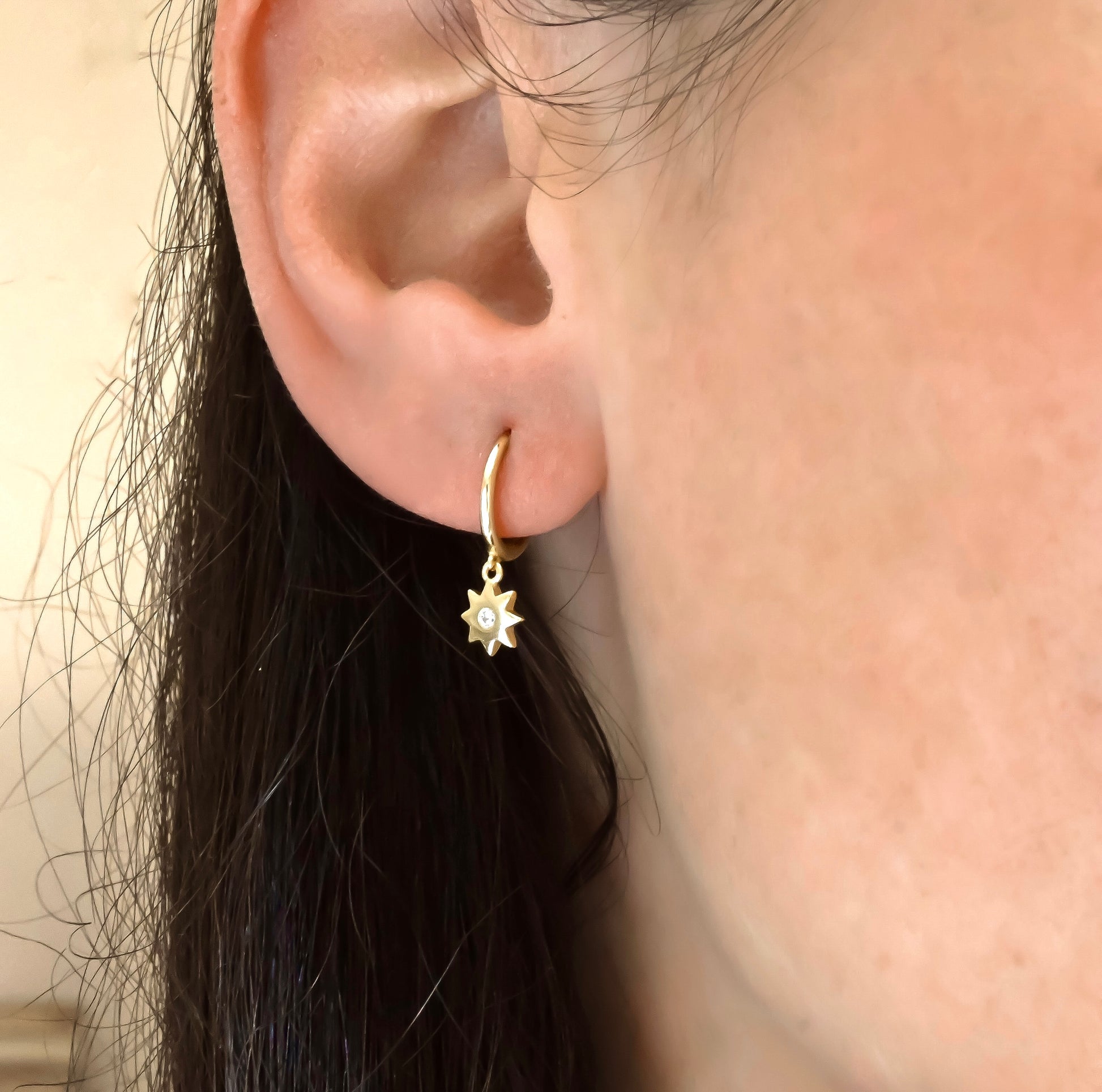 Close-up of an ear wearing a gold hoop earring with a star-shaped pendant.