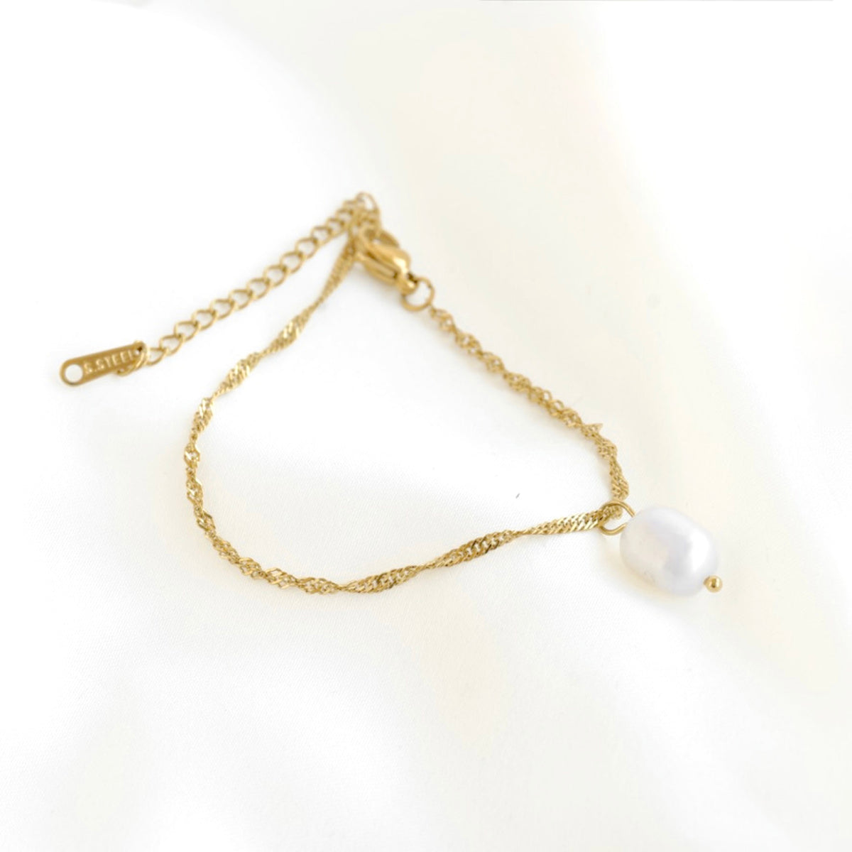 A delicate gold chain bracelet featuring a single irregular white freshwater pearl pendant, displayed on a soft white fabric background.