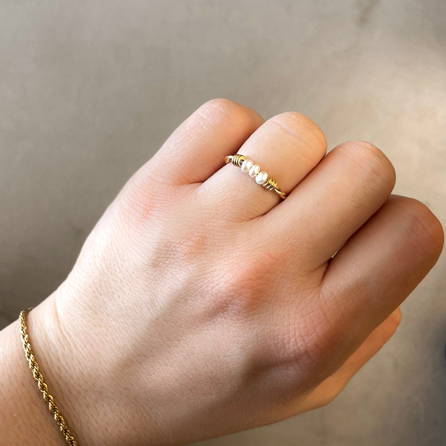 Hand wearing a slim twisted gold ring with small pearls on a neutral background