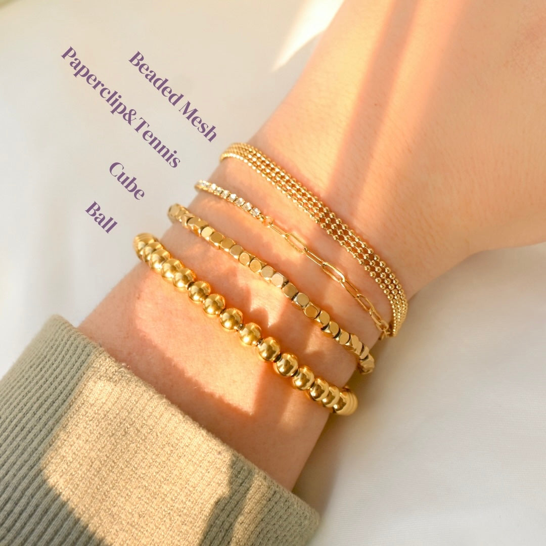 Gold beaded bracelets  with labels on a wrist with a neutral background