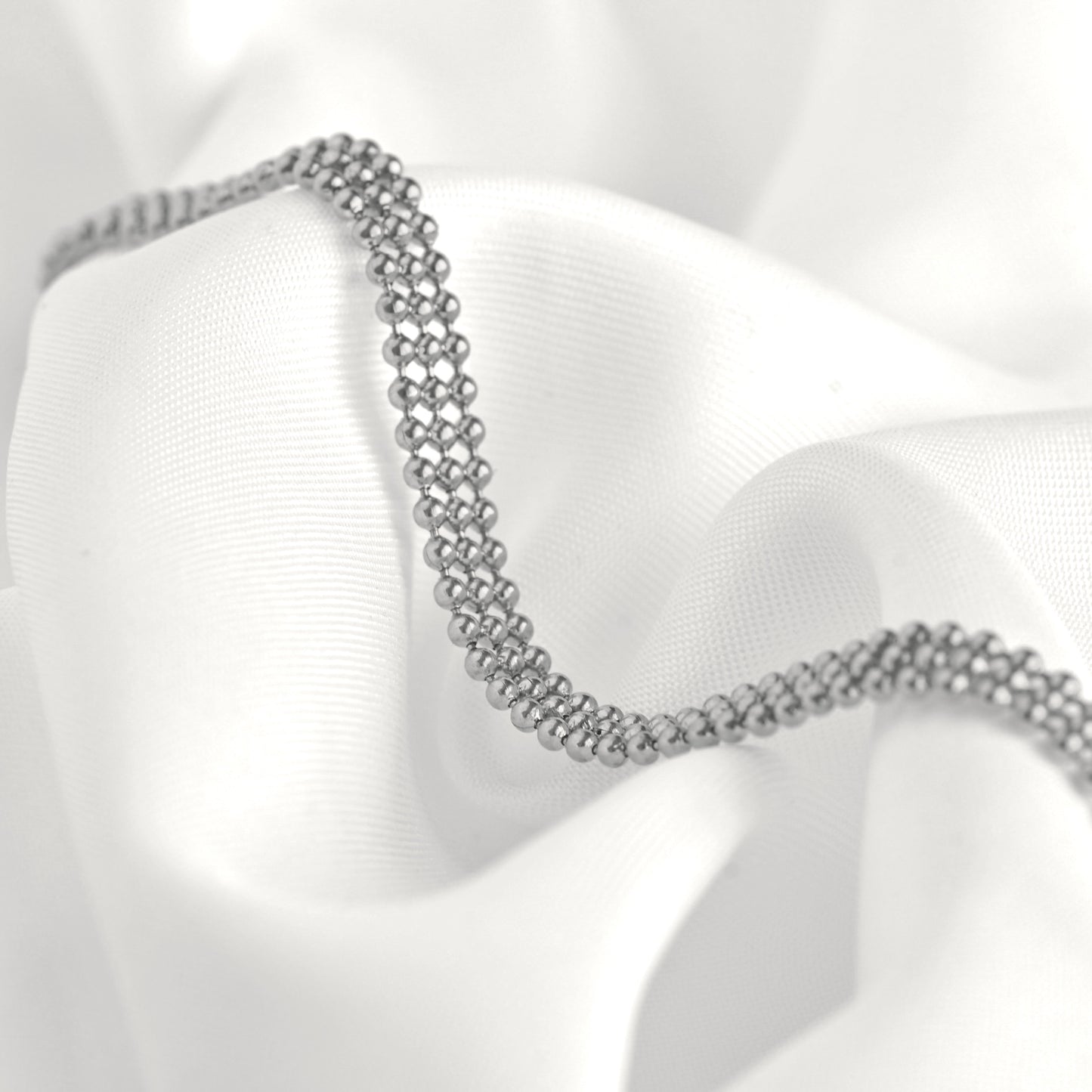 Silver beaded mesh bracelet on a white fabric background