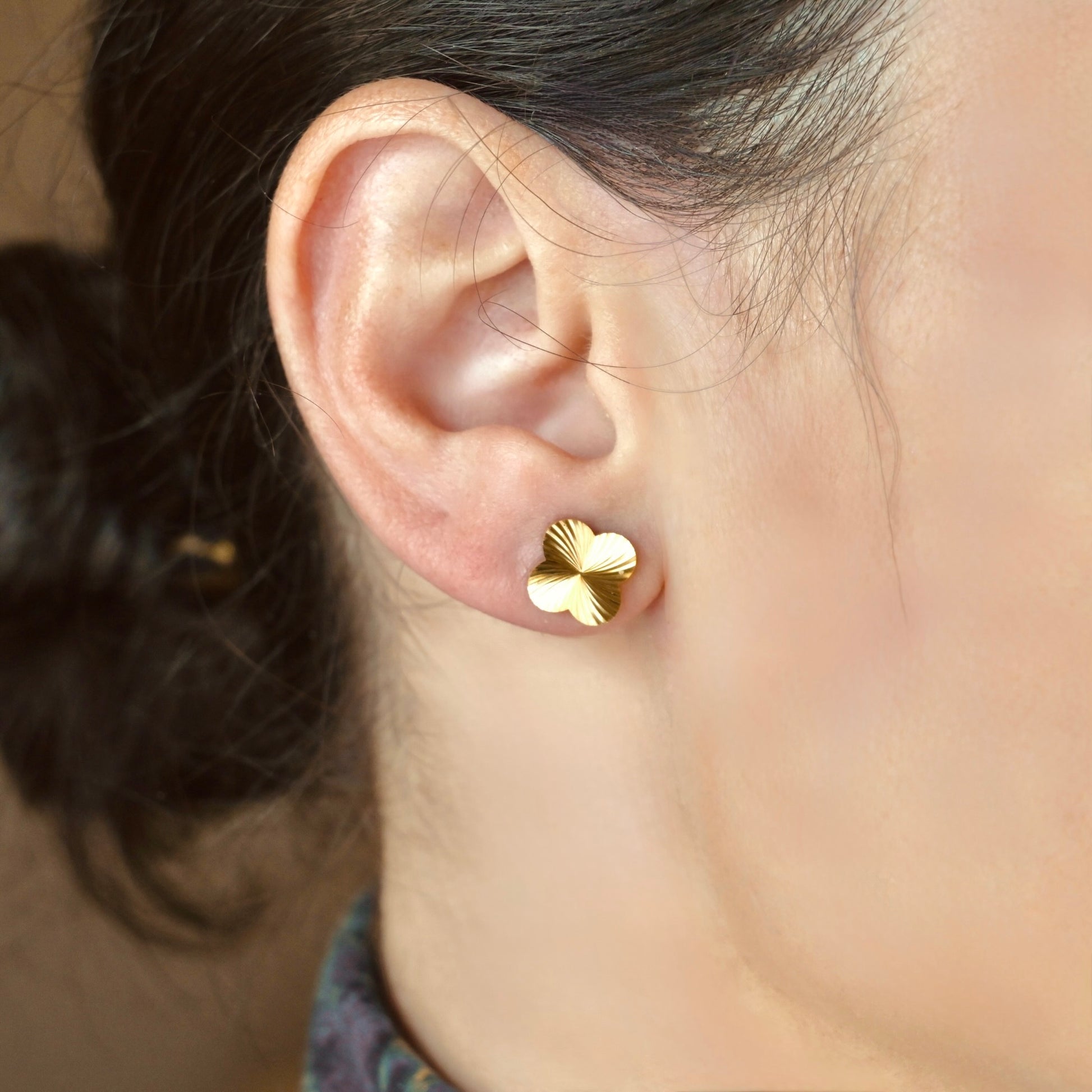 Gold four-leaf clover earring on a person's ear with a blurred background
