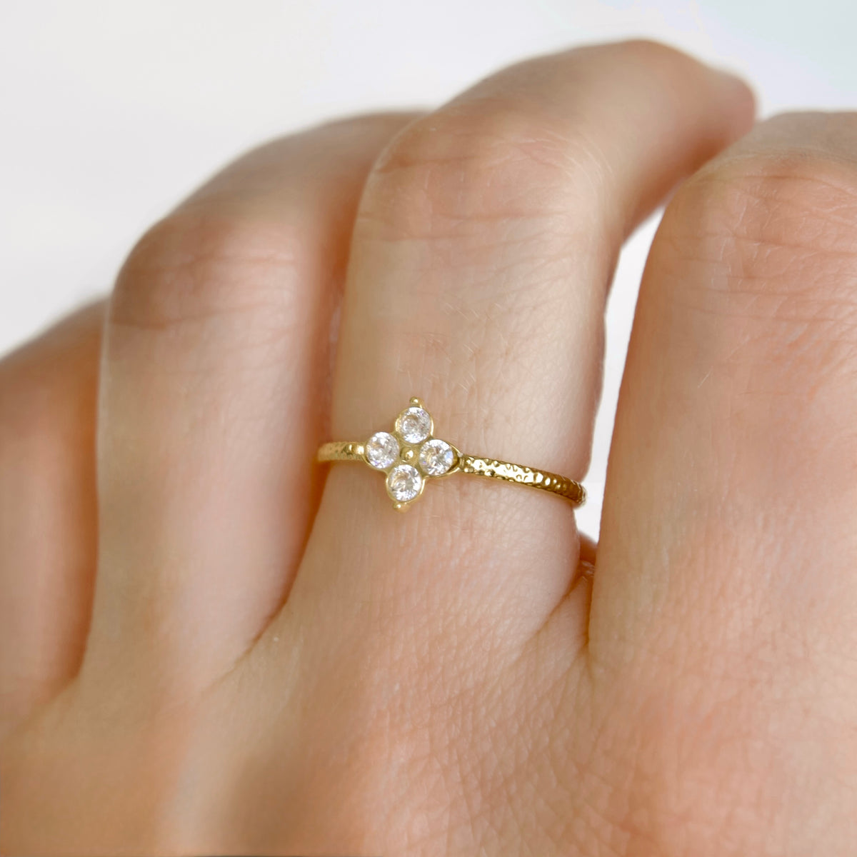 A delicate yellow gold ring with a small four-stone floral cluster featuring clear round-cut diamonds, shown worn on a finger.