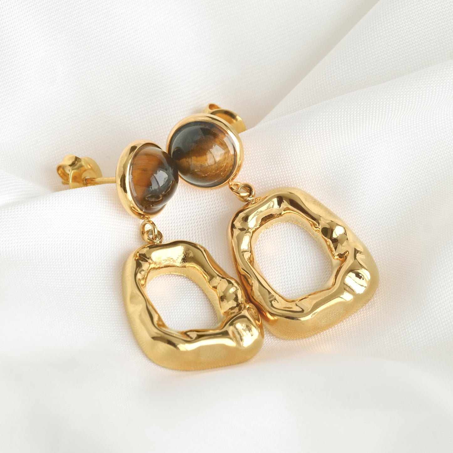 Gold dangles with hammered texture and  a central gemstone on a white background