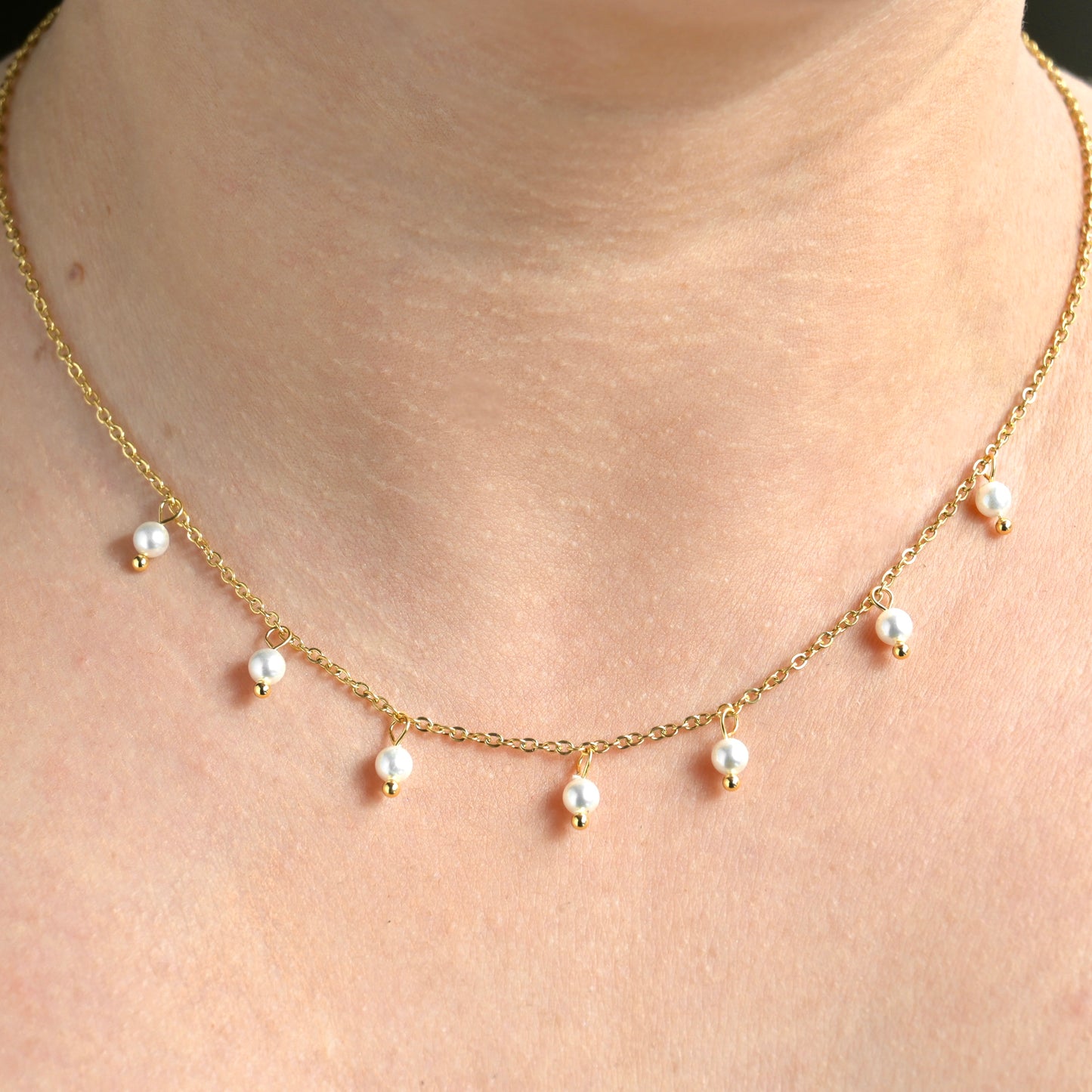 Gold necklace with pearl drops along a dainty cable chain on a person's neck