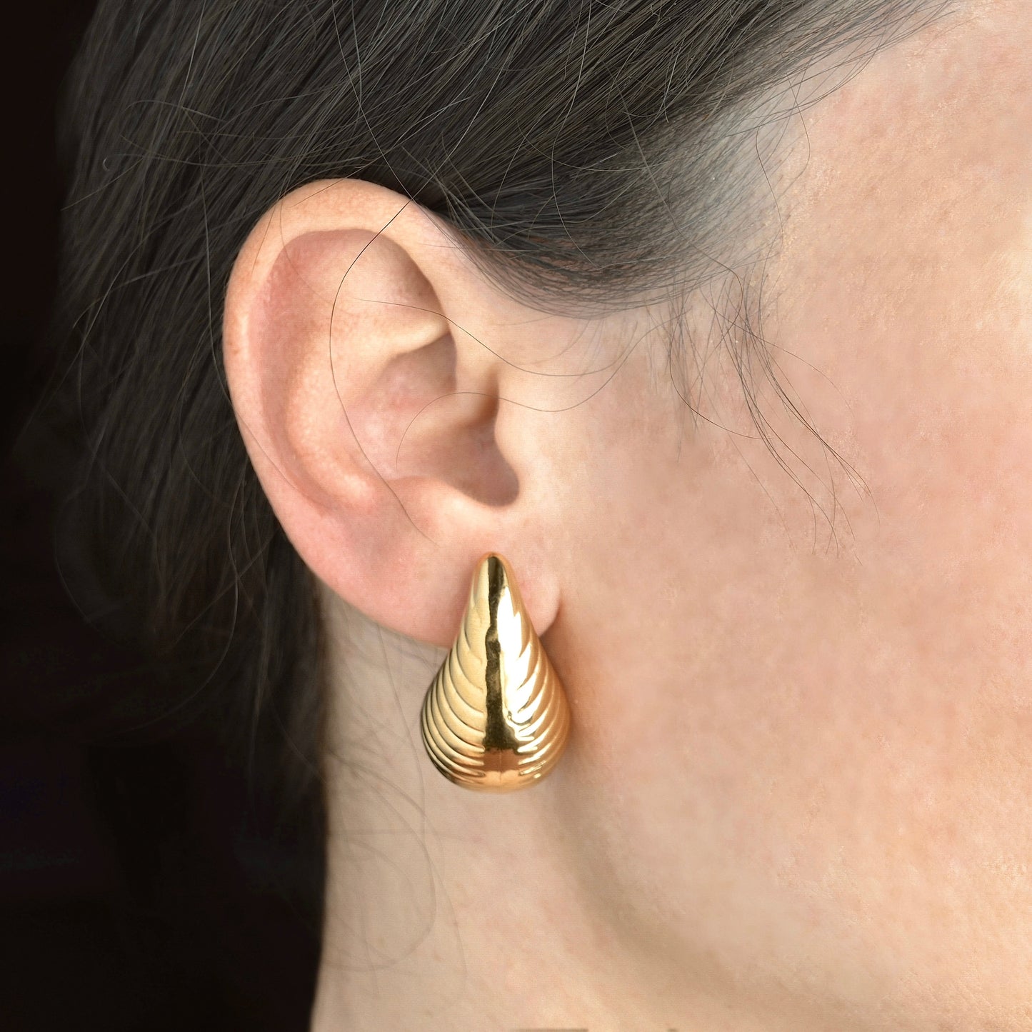 Chunky teardrop earring worn by a person with dark hair.