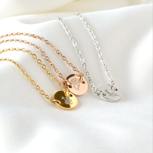 Three bracelets with round birth flower charms in gold, rose gold and silver on a white surface