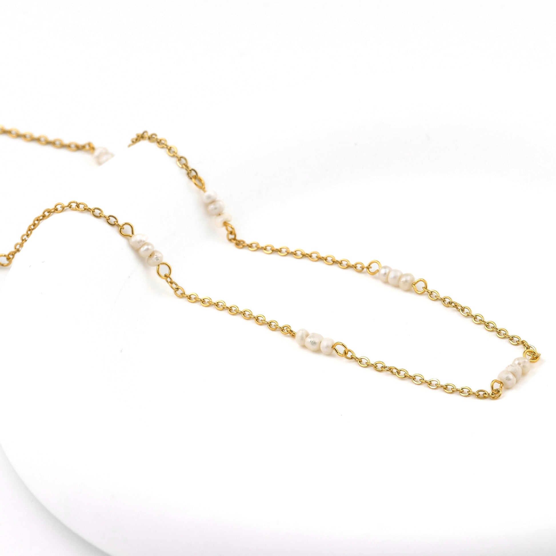 Gold chain necklace with tiny pearls on a white background