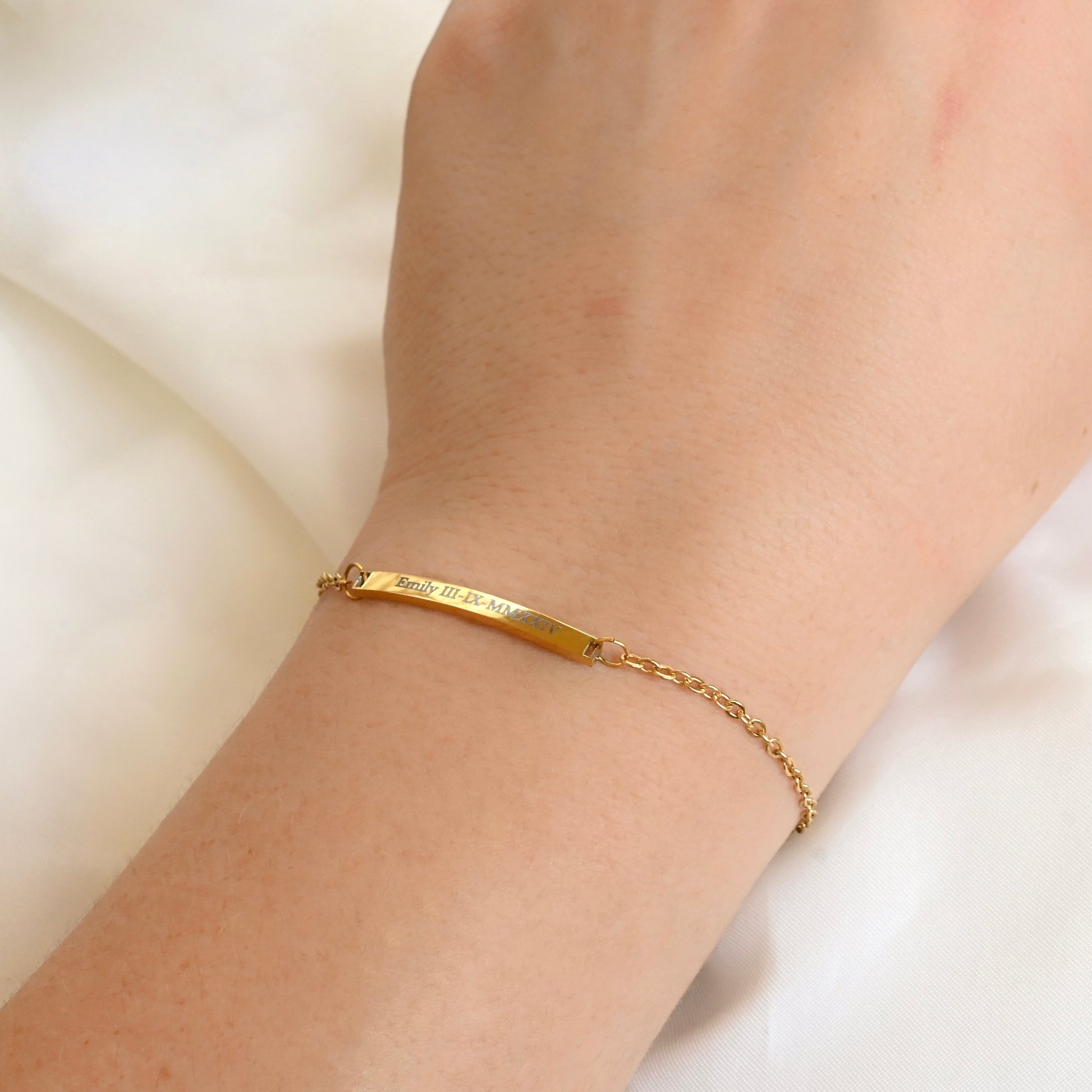 Gold bracelet with custom roman numeral engraving on a wrist with a plain background