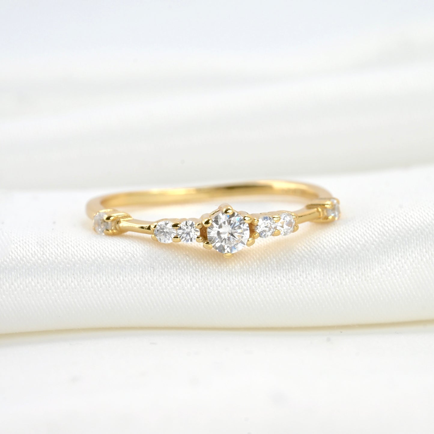 Front view of gold ring with  small and medium sized CZ stones on a white fabric background