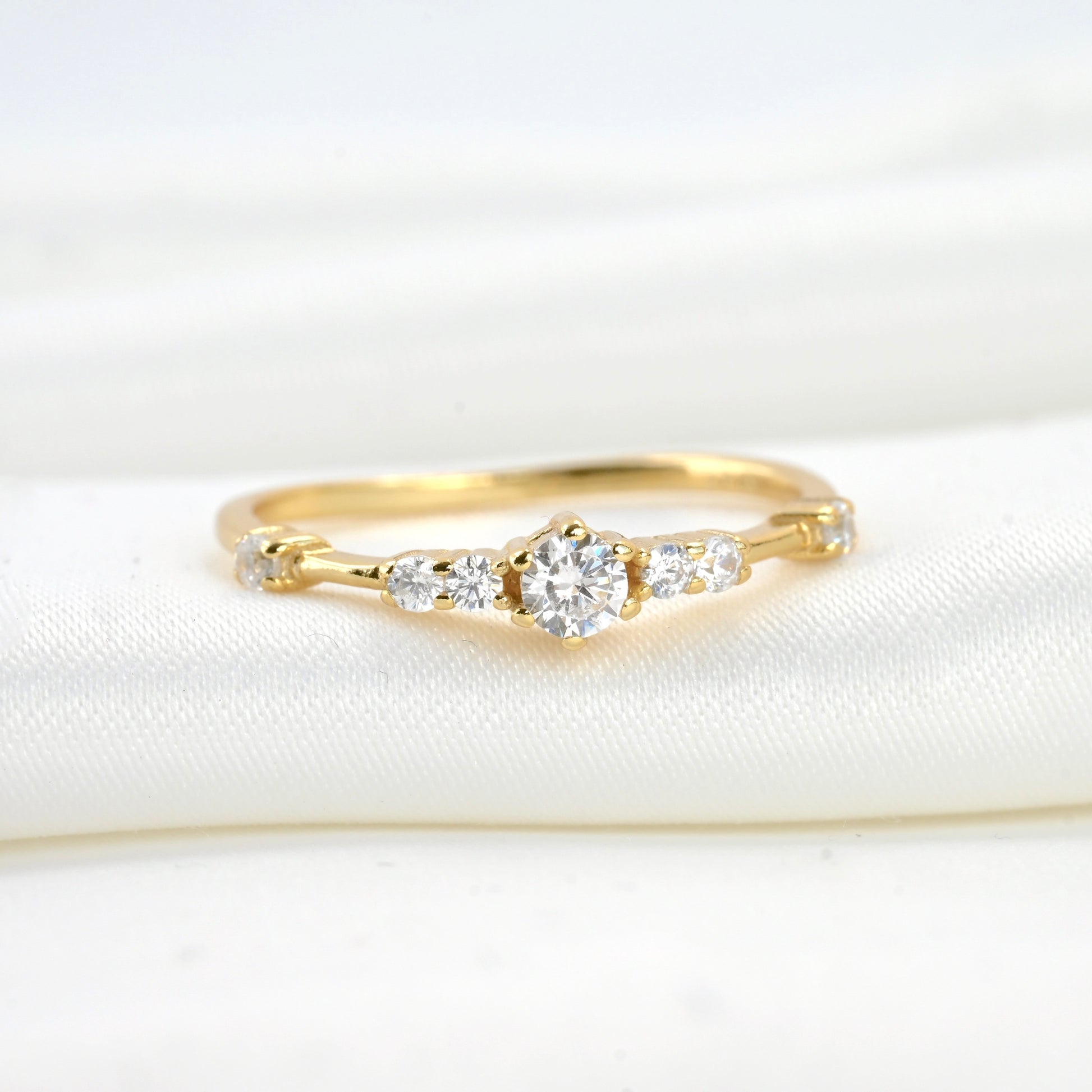 Front view of gold ring with  small and medium sized CZ stones on a white fabric background