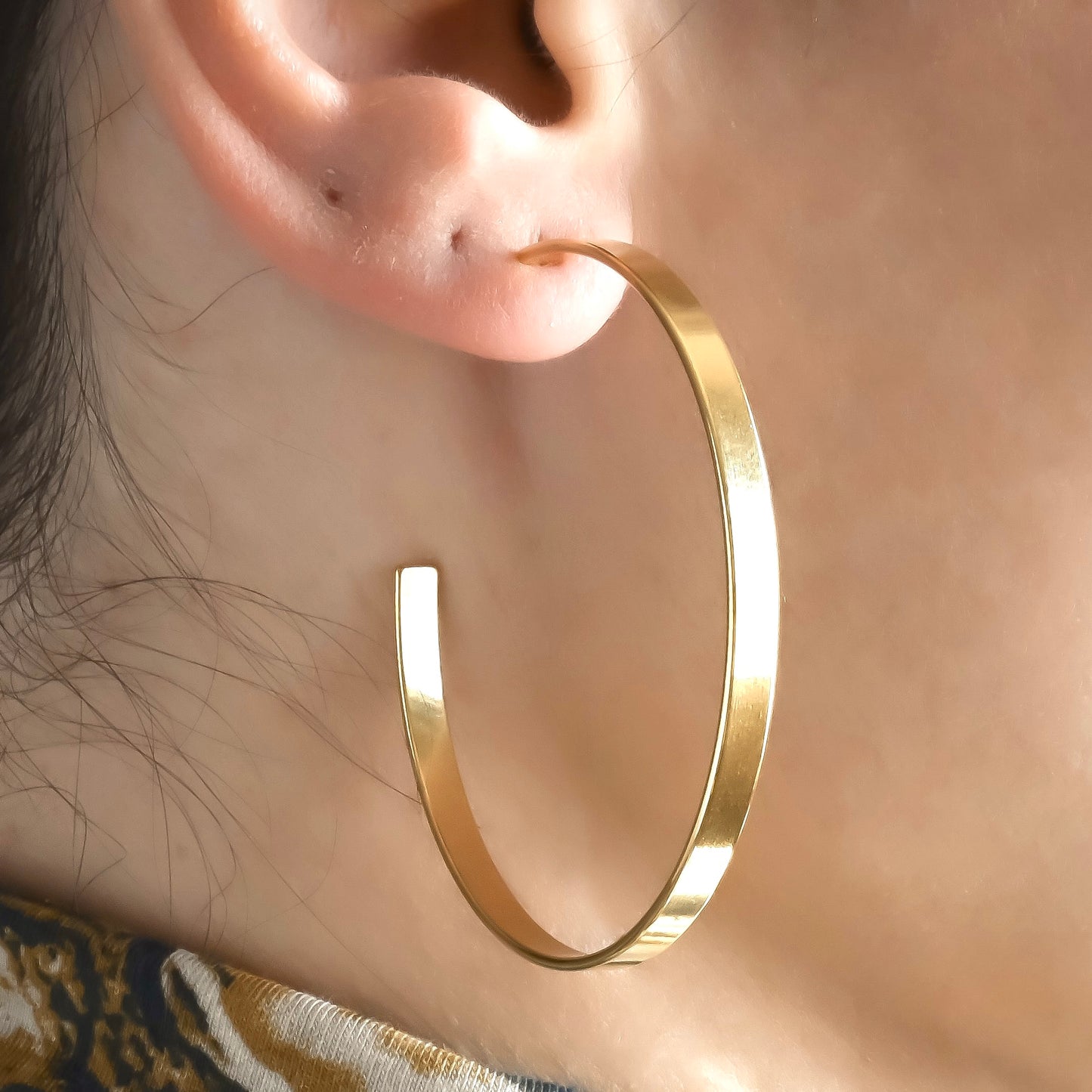 Side view of flat gold C hoop earrings worn by a person with a neutral background