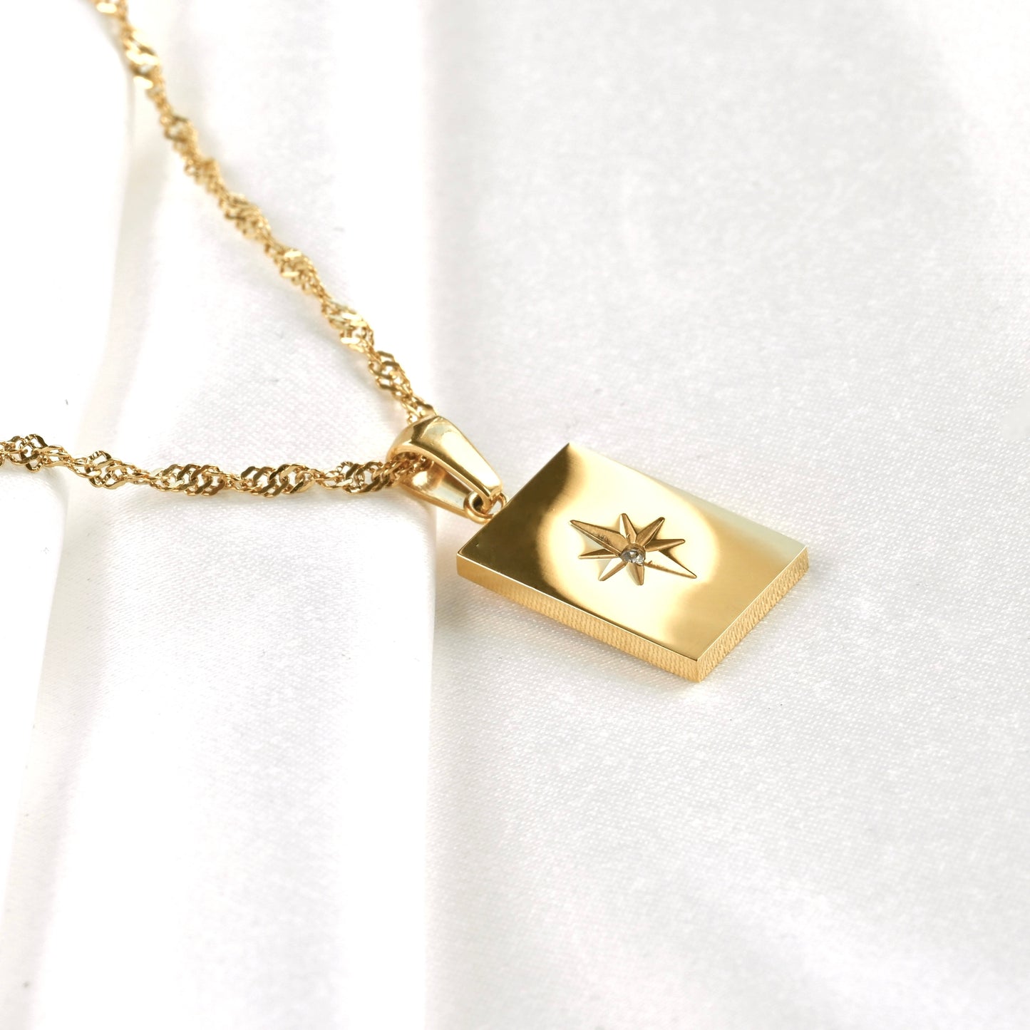 Gold rectangular starburst necklace with a singapore chain featuring a star design with a tiny CZ centerpiece on a white background