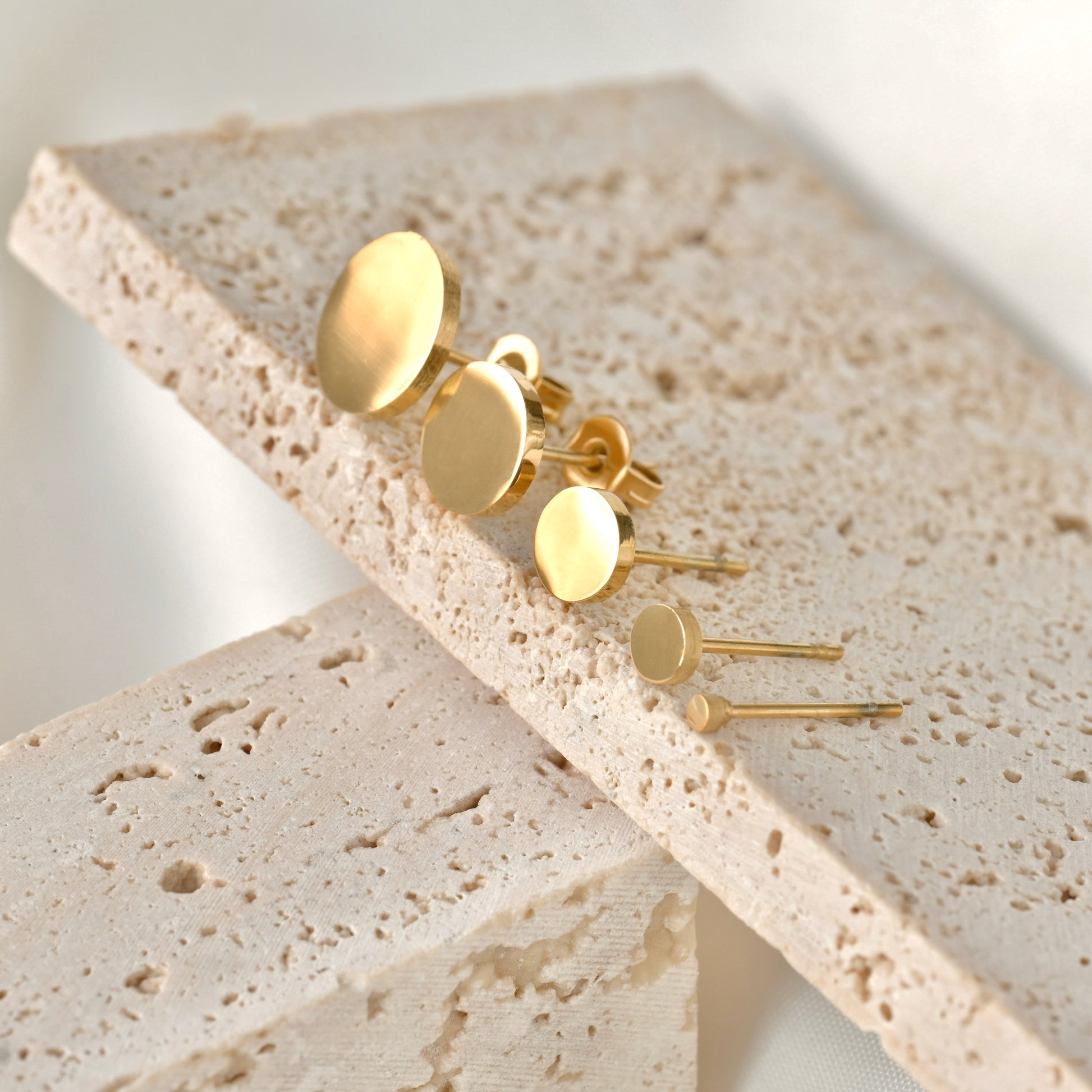 Gold disc stud earrings on a textured stone surface