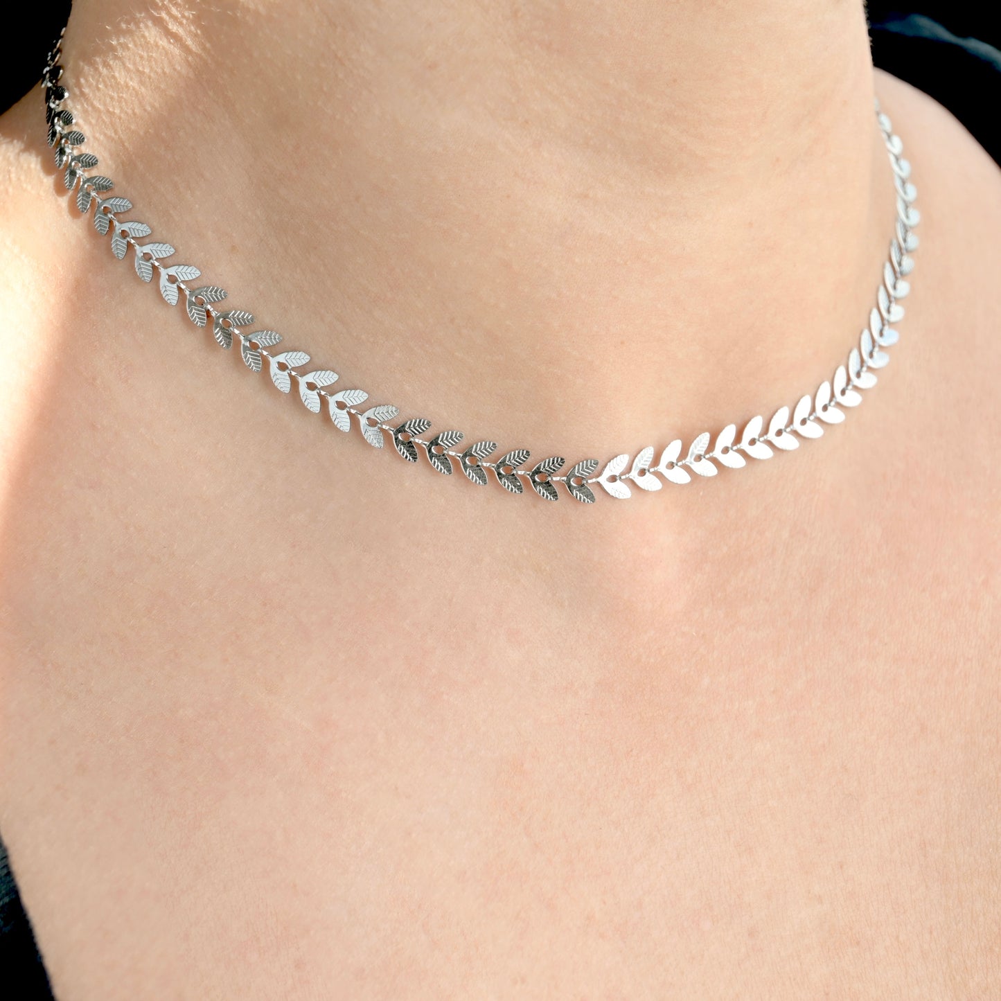Silver leaf-patterned necklace on a person's neck against a neutral background