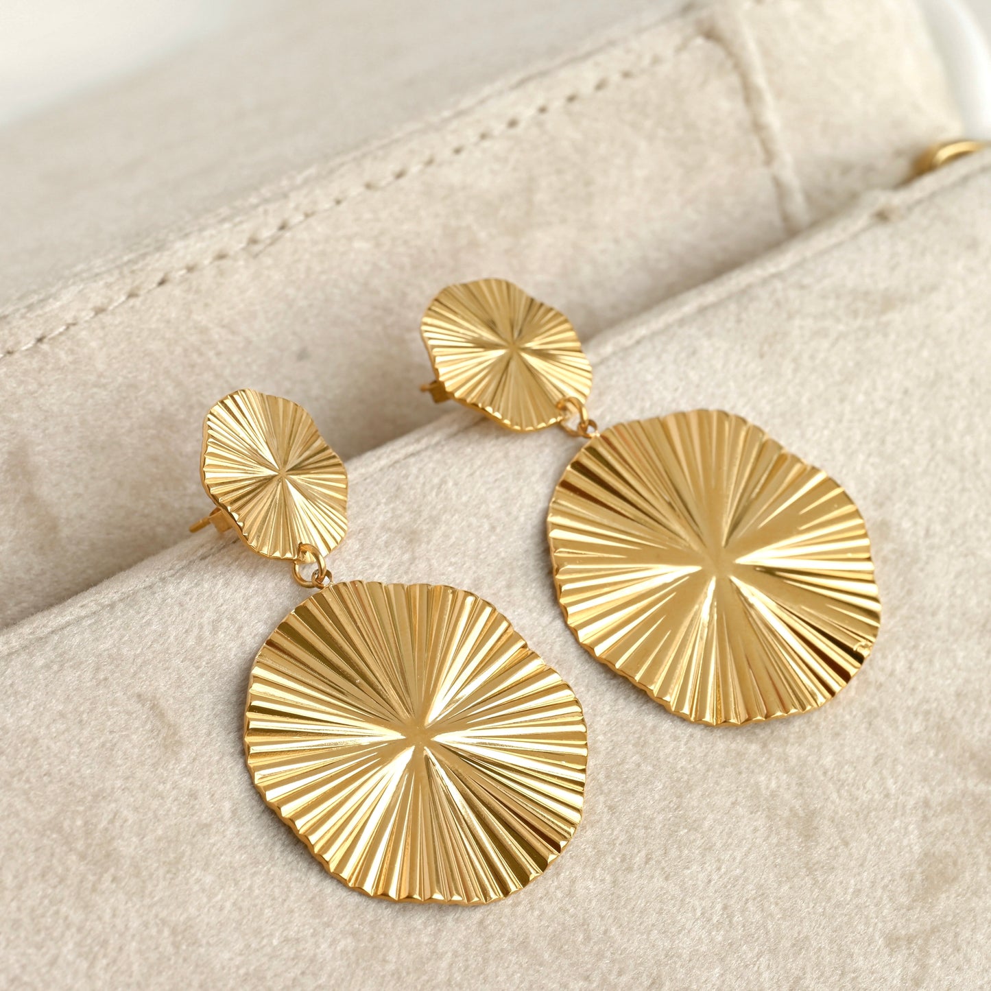 Gold earrings with sunburst design on a beige surface