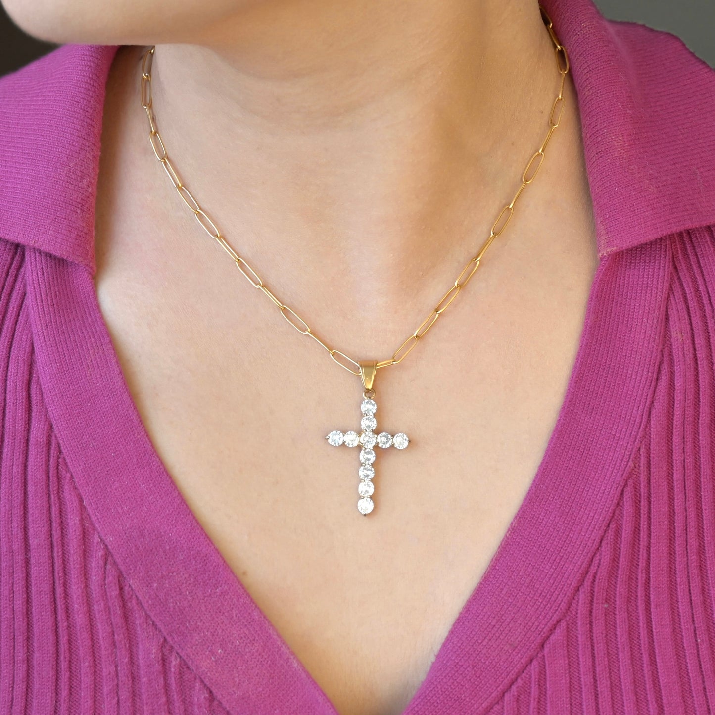Gold cross necklace with diamonds worn by a person in a pink top.