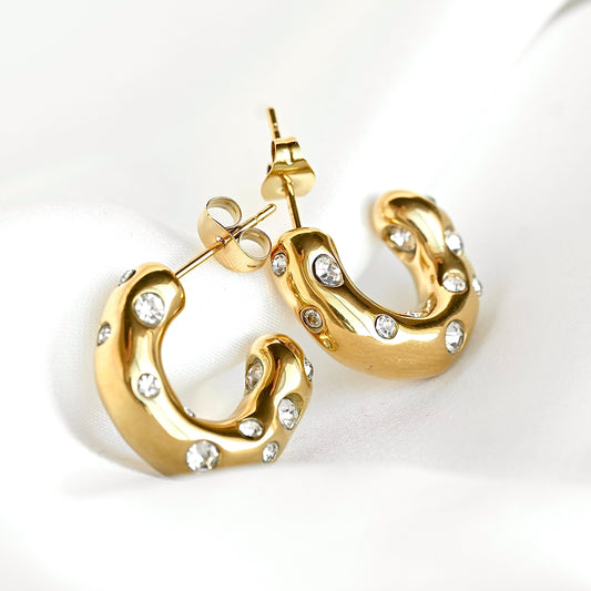 A pair of gold crescent-shaped hoop earrings embellished with small clear stones, displayed on a clean white background.