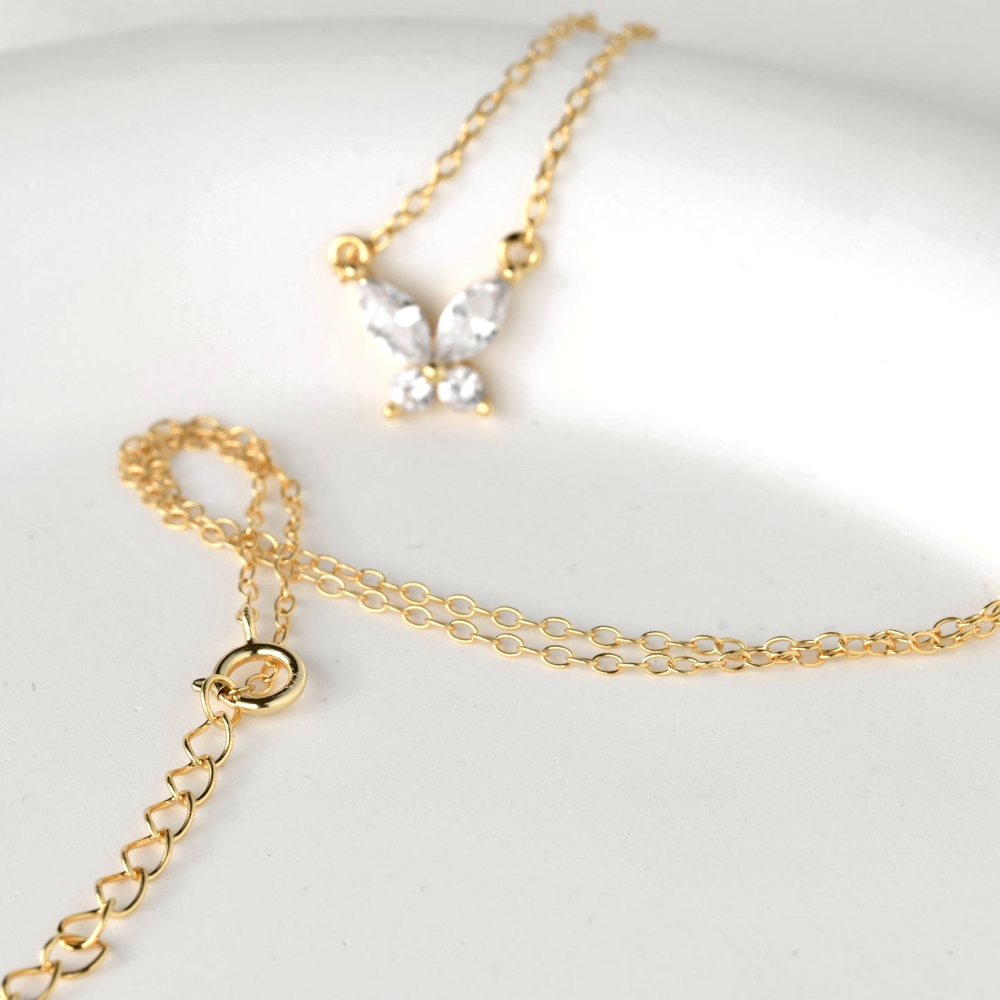 Gold butterfly necklace with a spring ring clasp with S925 stamp and an exender on a light gray background