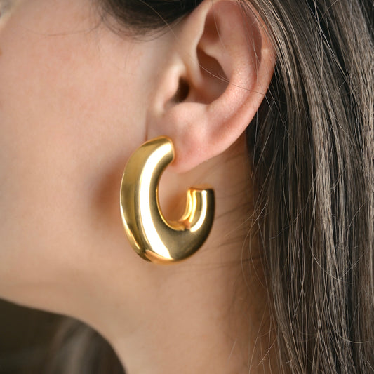 Oversized statement Gold hoop earring worn by a person with brown hair.