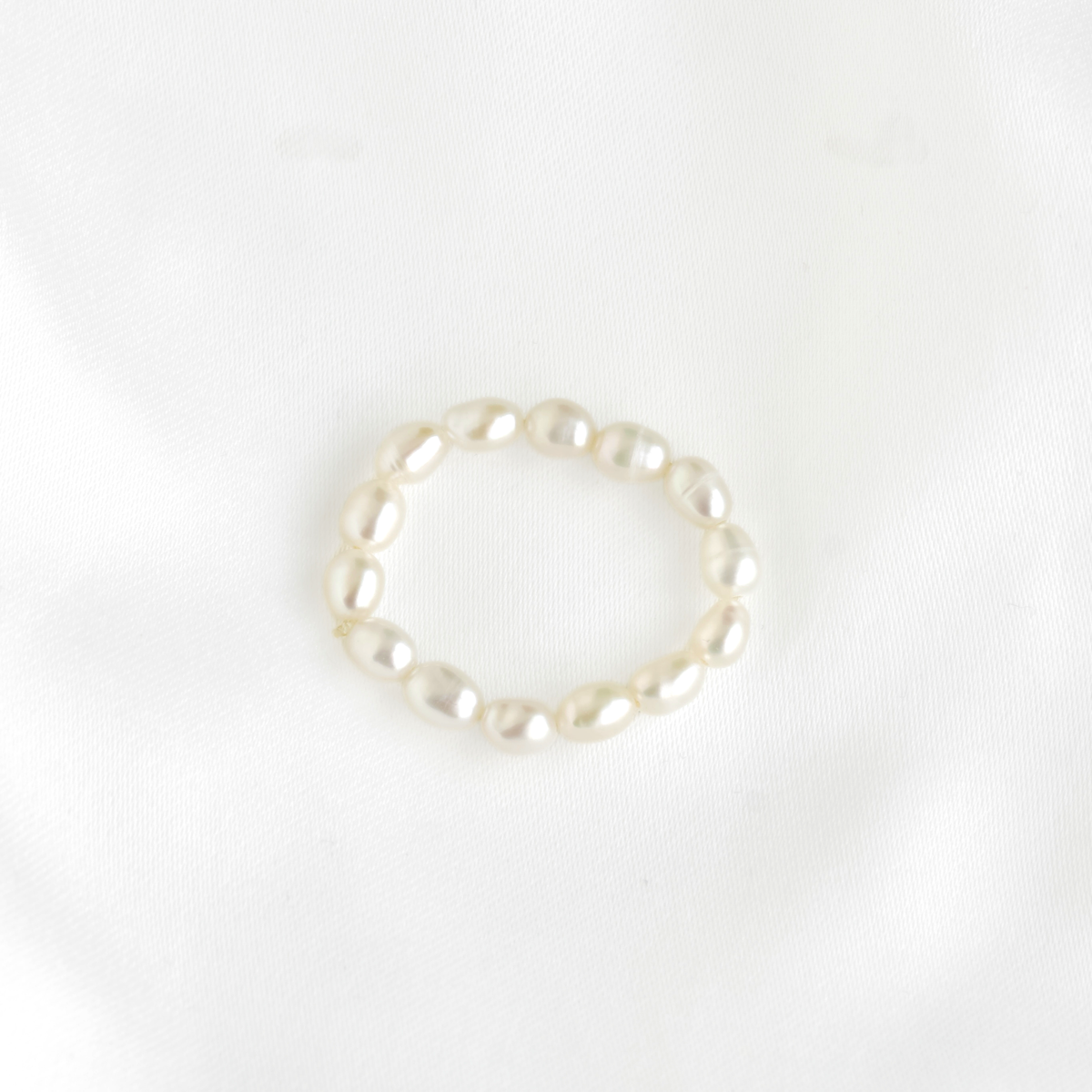 A single ring made of irregular white pearls, photographed on a soft white fabric background.