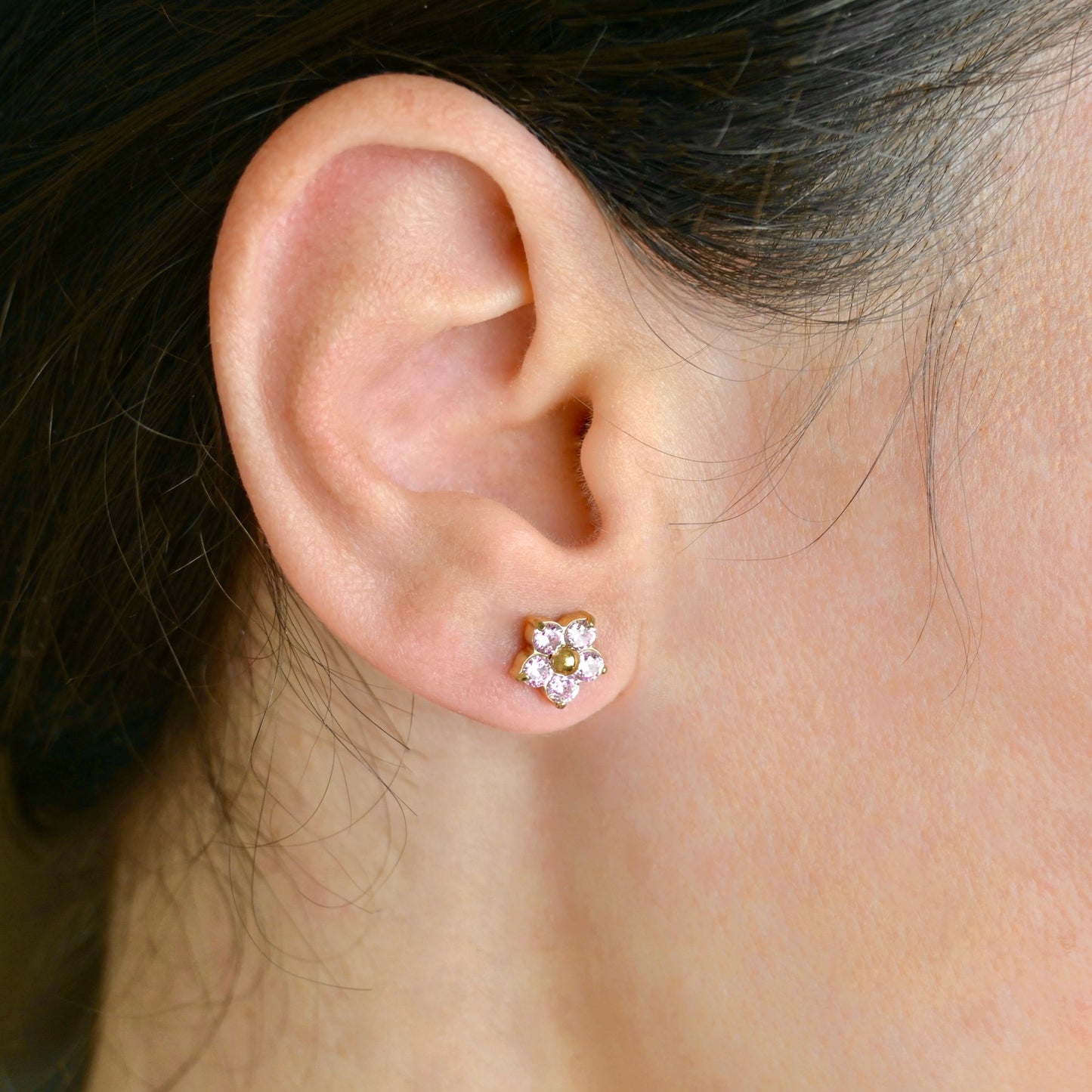 Small gold flower studs with pink CZ petals worn by a person