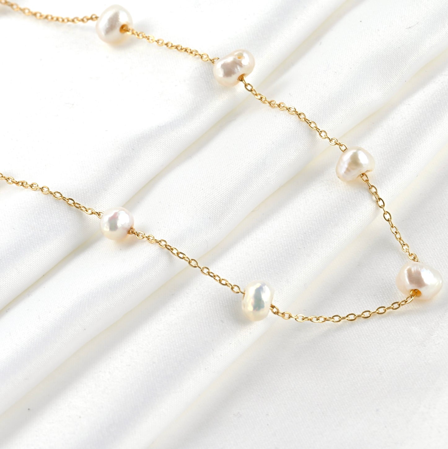 Gold necklace with natural baroque pearls stationed along a delicate cable chain on a white background