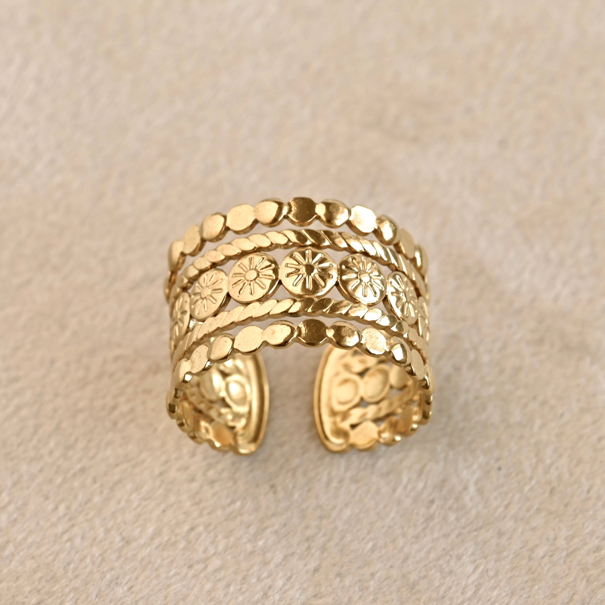 Stacked gold open ring with intricate design on a beige background