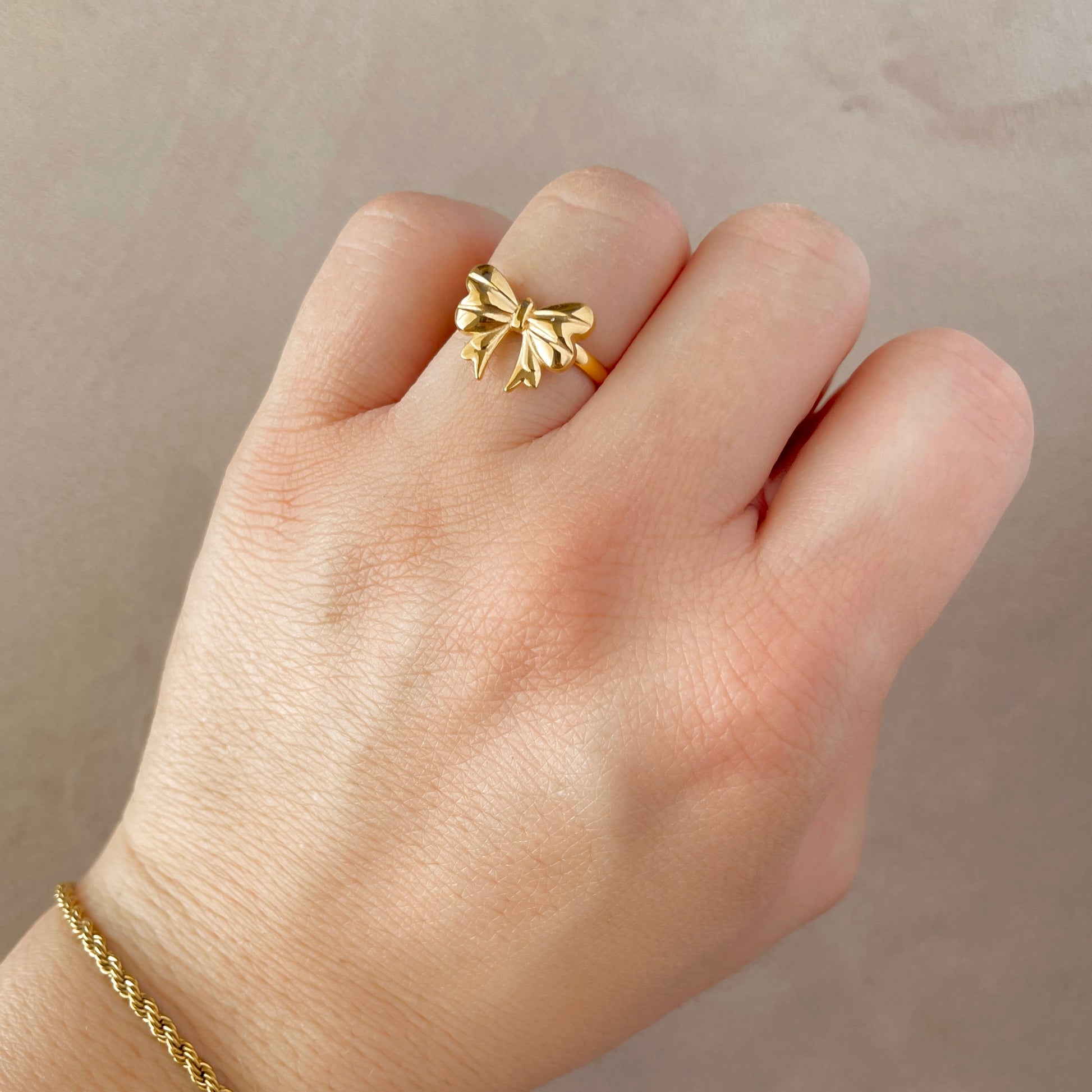 Gold ring with bow design on a hand against a neutral background