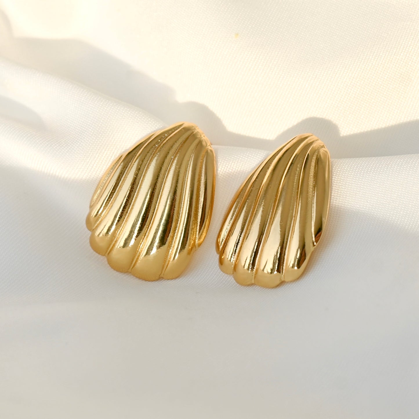 Gold shell-shaped earrings on a light fabric background