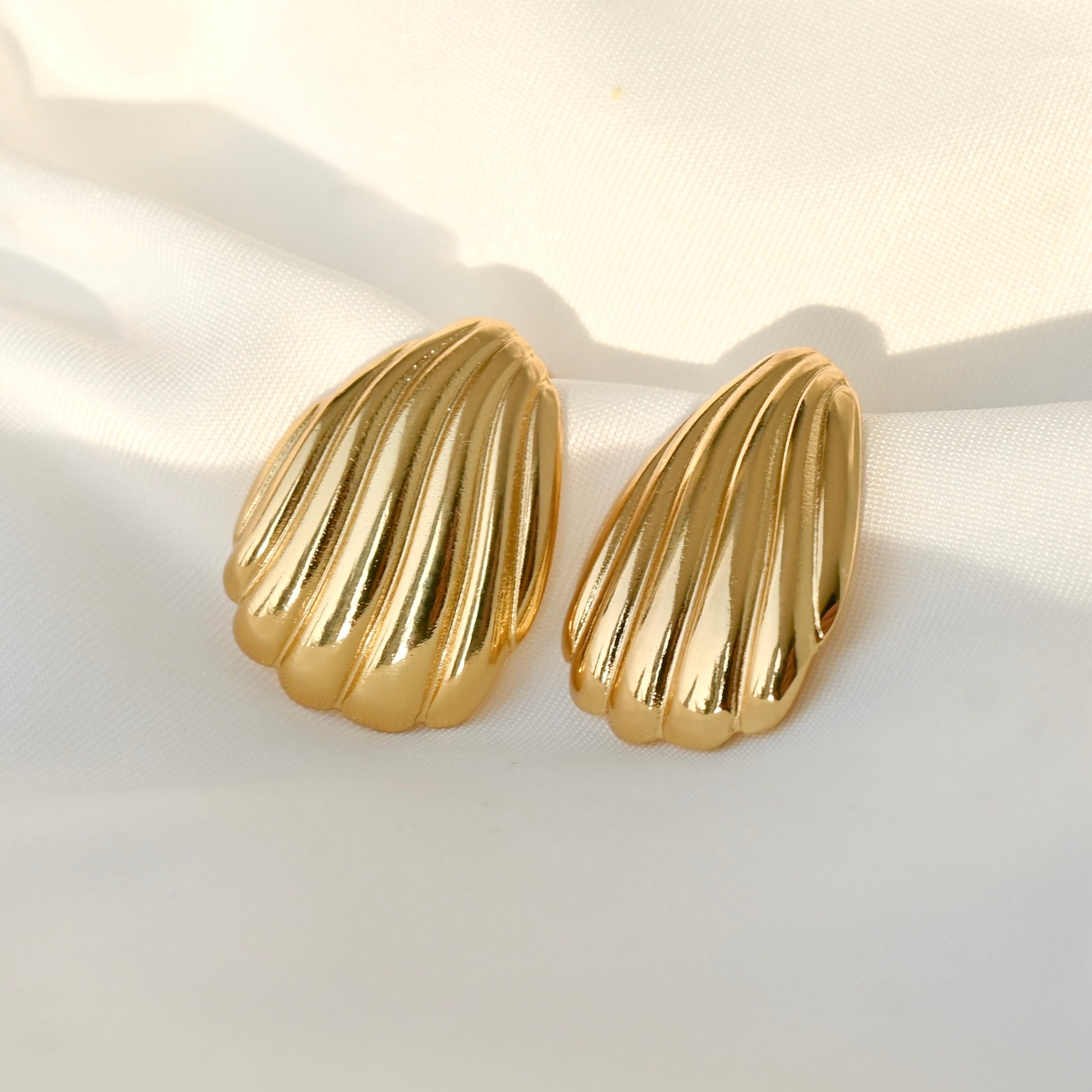 Gold shell-shaped earrings on a light fabric background