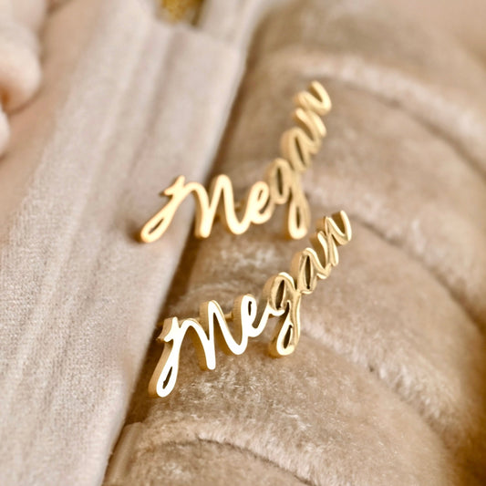 Gold 'Megan' name ring on a beige fabric background
