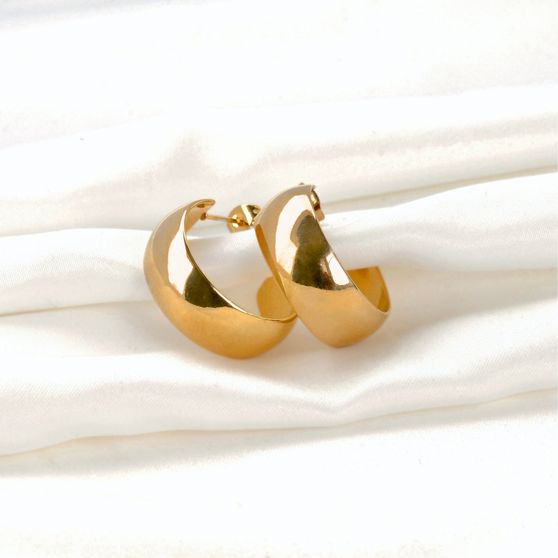 Wide gold C hoop earrings on a white background