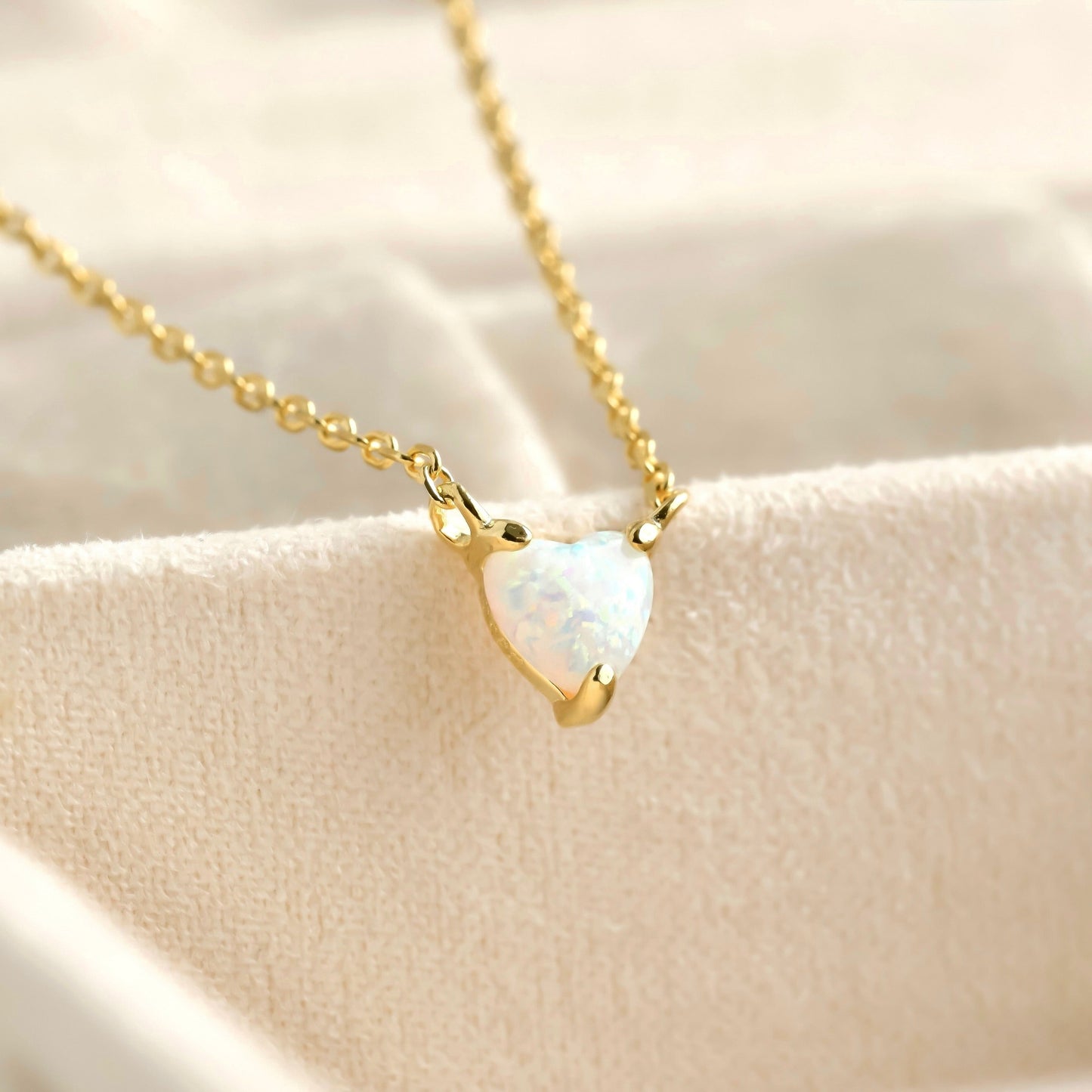 Gold opal heart necklace on a beige background