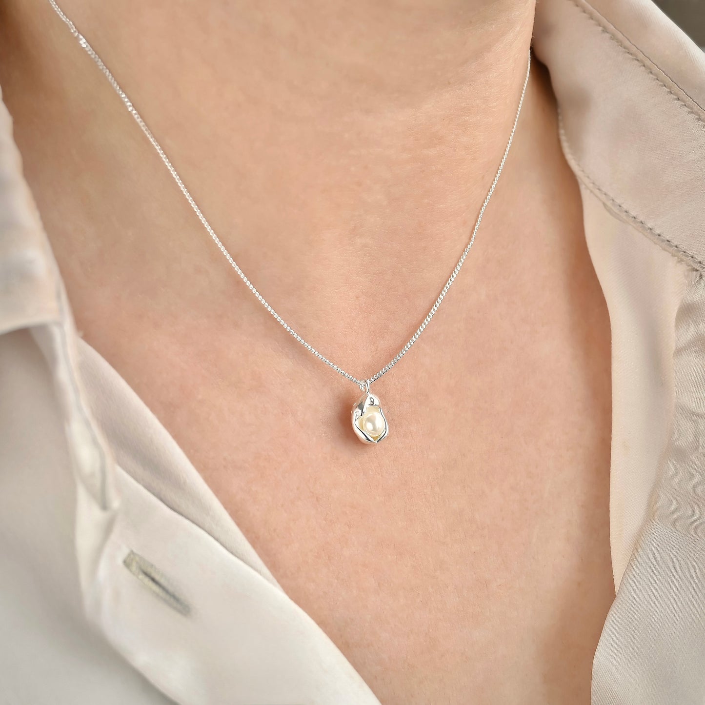 Silver oyster necklace with a fine curb chain on a person wearing a light-colored shirt.