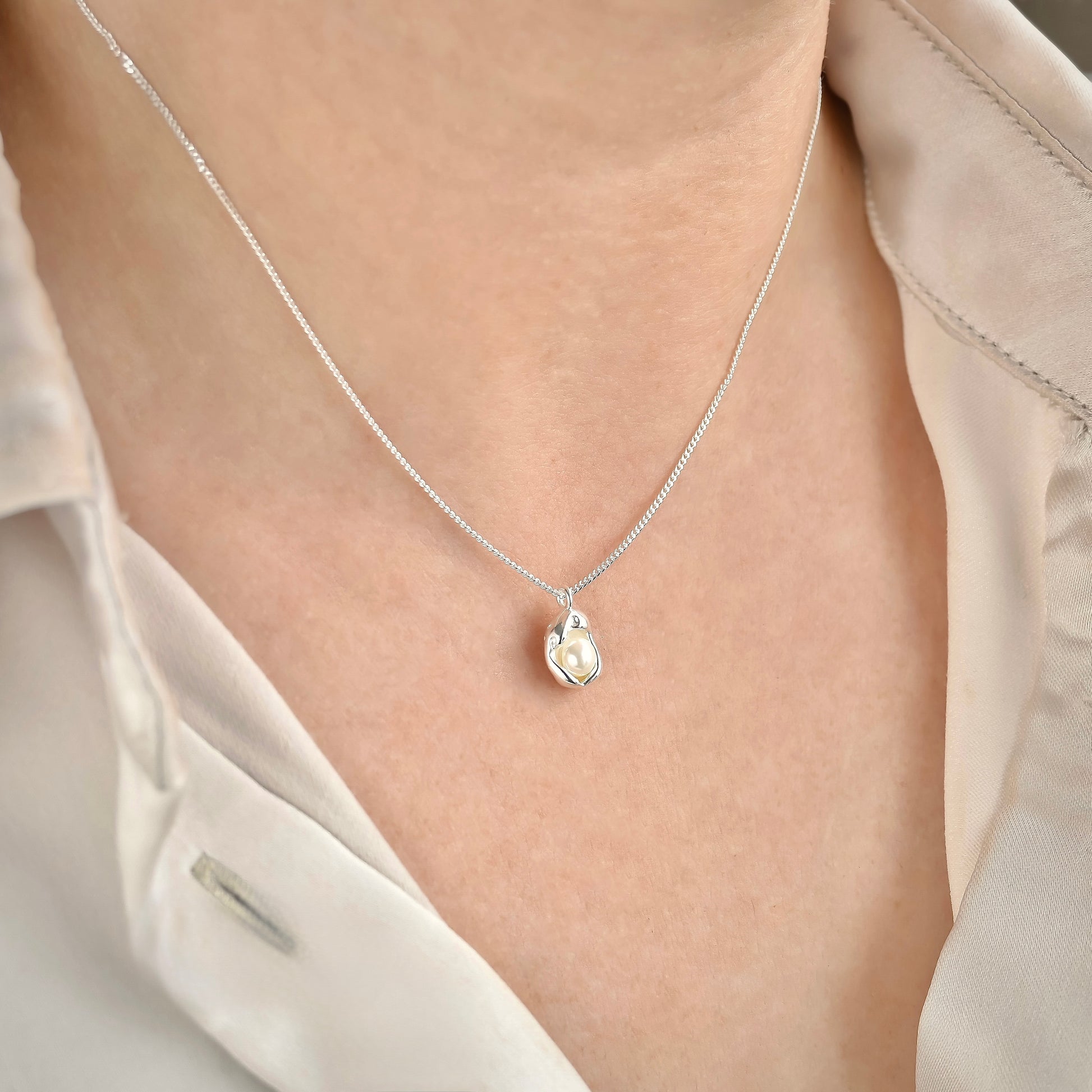 Silver oyster necklace with a fine curb chain on a person wearing a light-colored shirt.