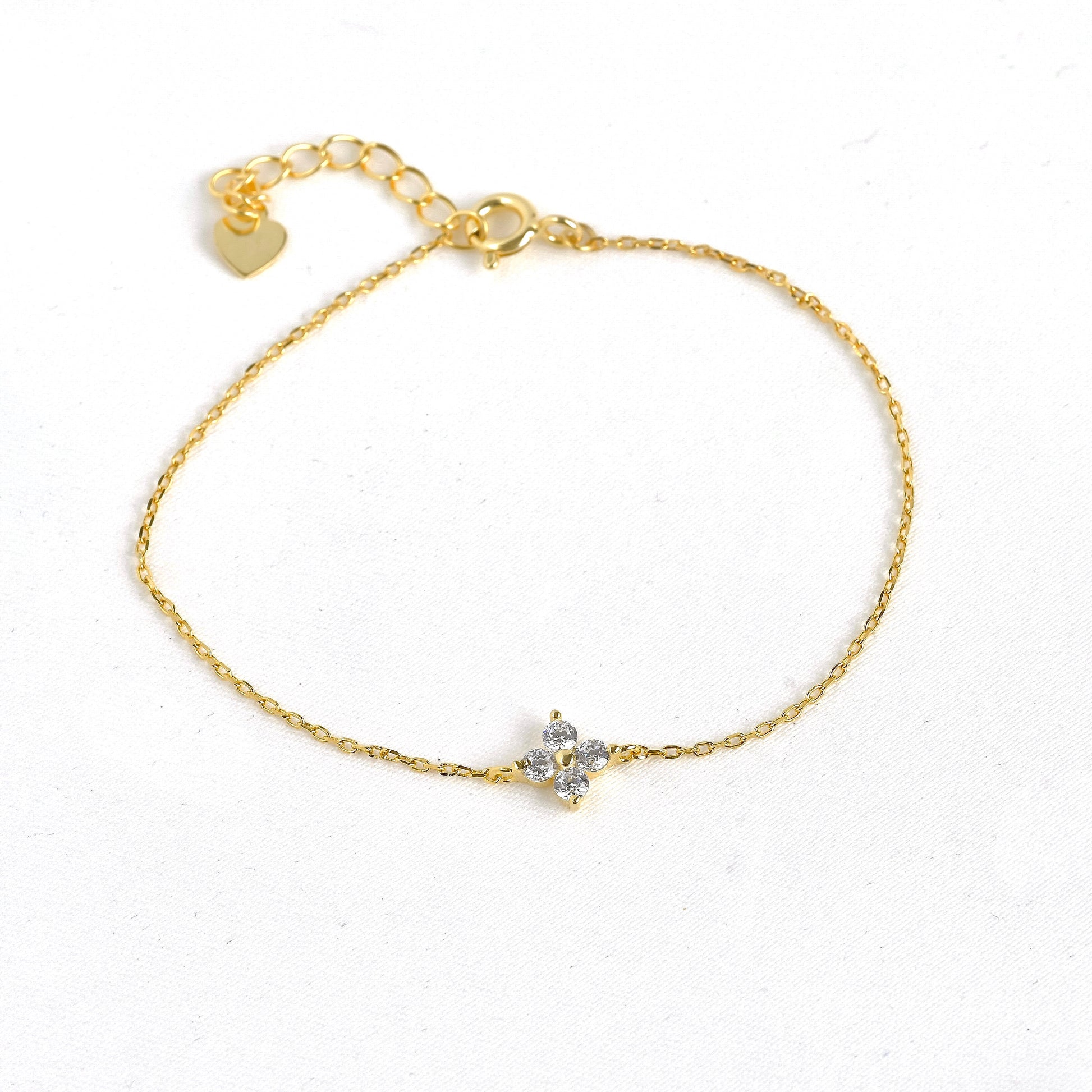 Top view of gold 4 leaf clover CZ bracelet with a small heart charm on a white background