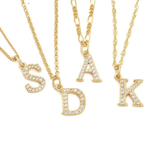 Five gold necklaces with CZ letter pendants on a white background. From left to right: curb chain with 'S', rolo with 'D', figaro with 'A', and singapore with 'K'.